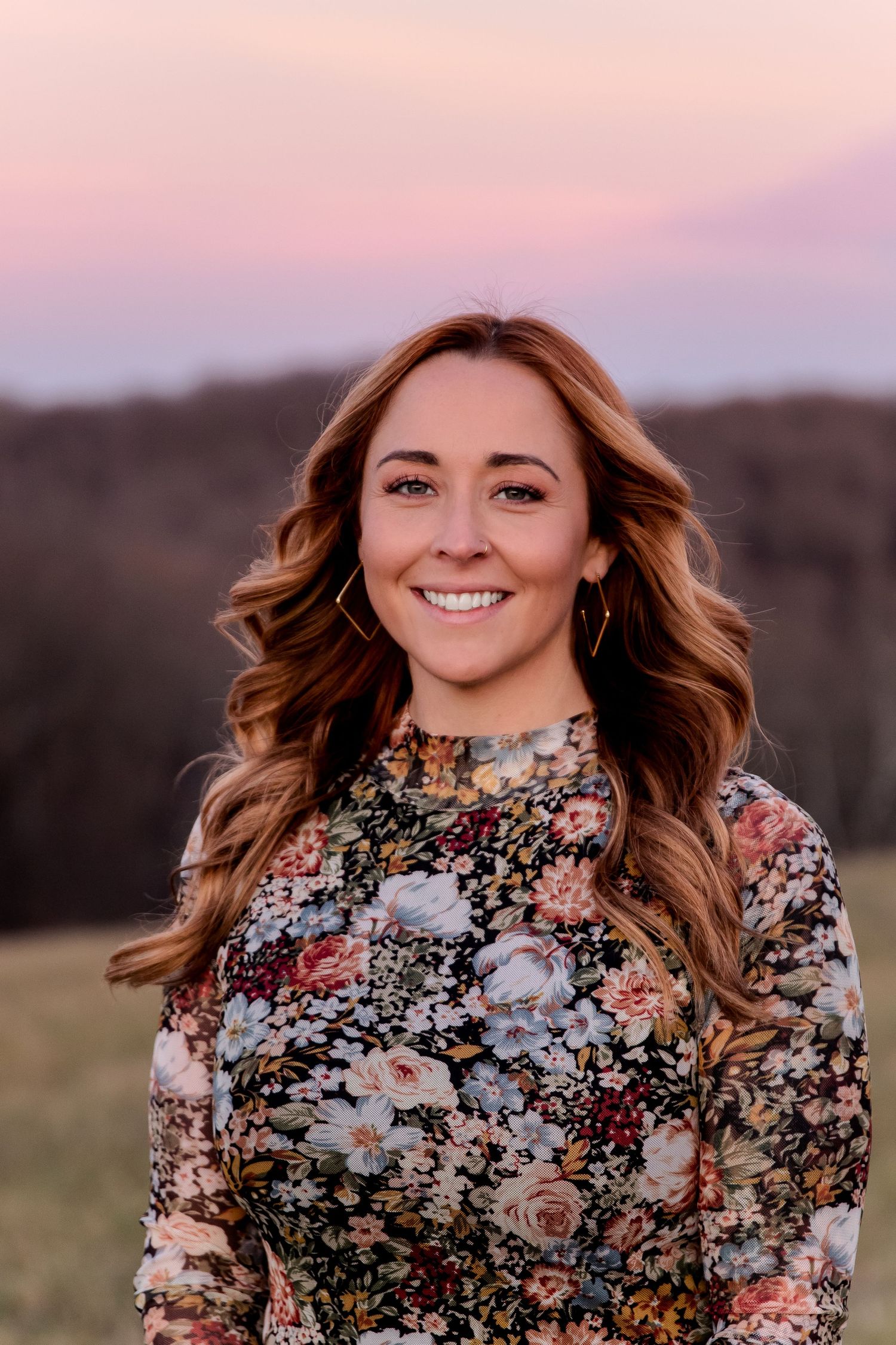 Portrait of someone in a floral dress against a sunset landscape background with long flowing hair.