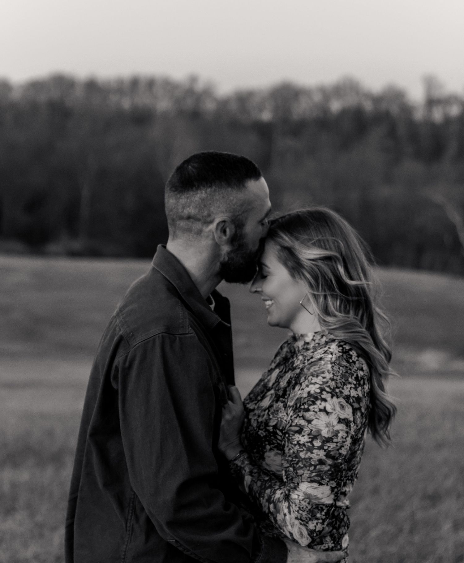 Black and white photo of a romantic couple sharing an intimate moment in an open field at dusk.