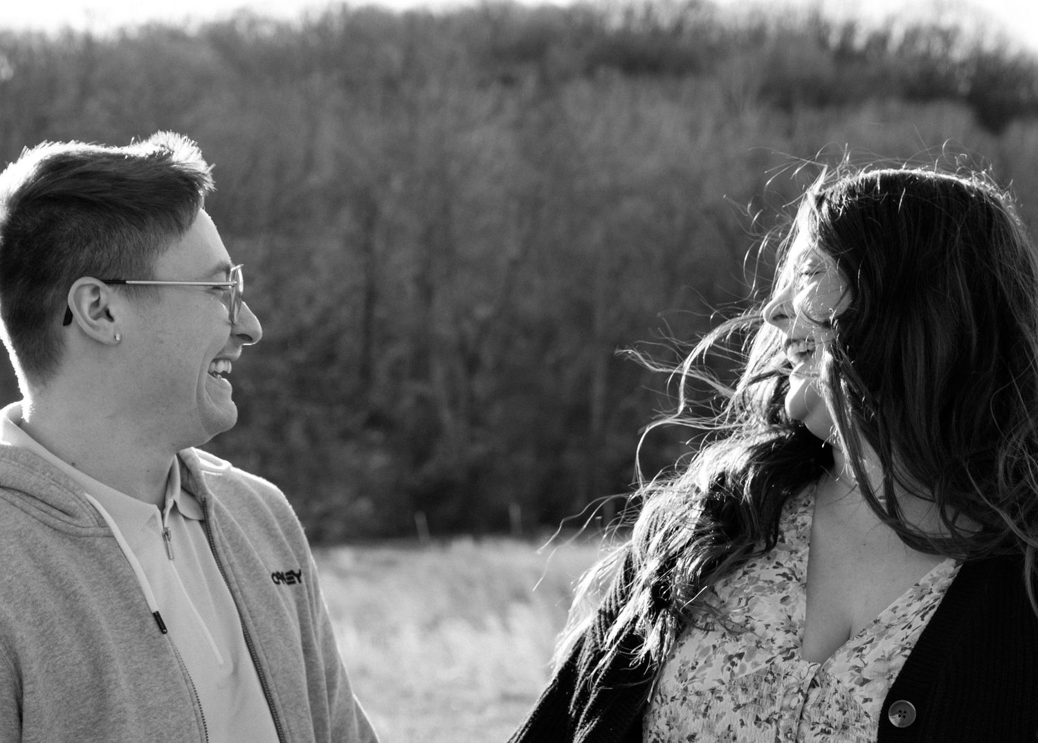 A couple shares an intimate black and white moment in a field with trees in the background.
