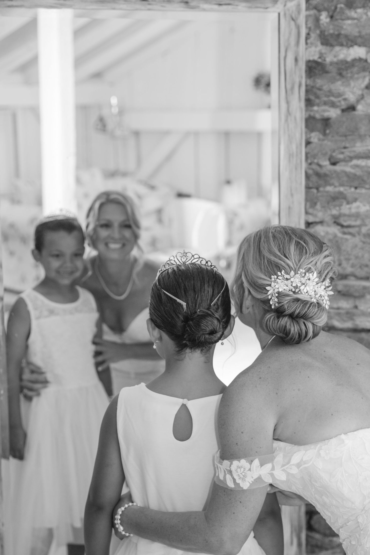 Row of bridesmaids shown from behind wearing white dresses and crystal hair accessories at a wedding.