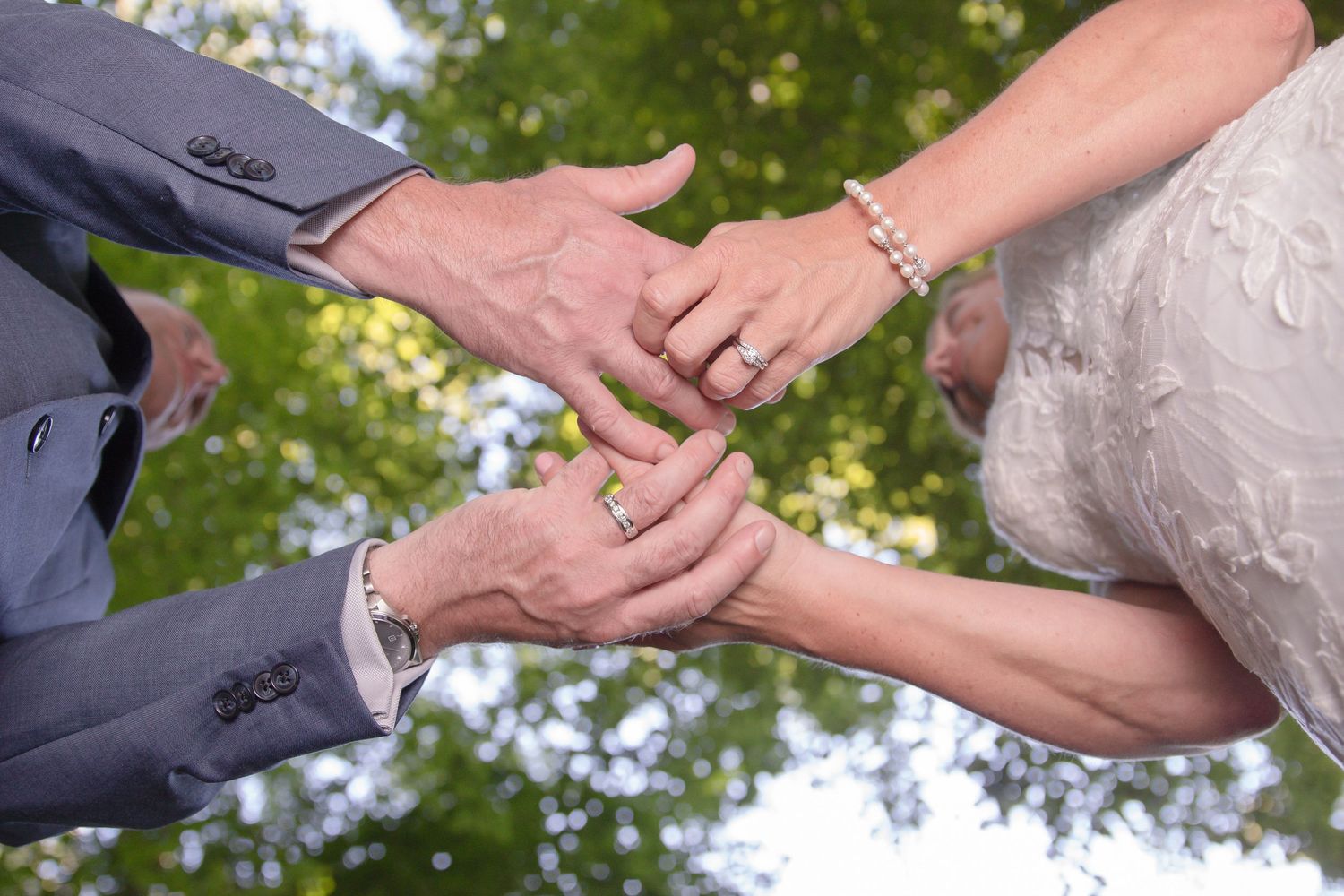 A person places a wedding ring on another person's finger during an outdoor wedding ceremony.