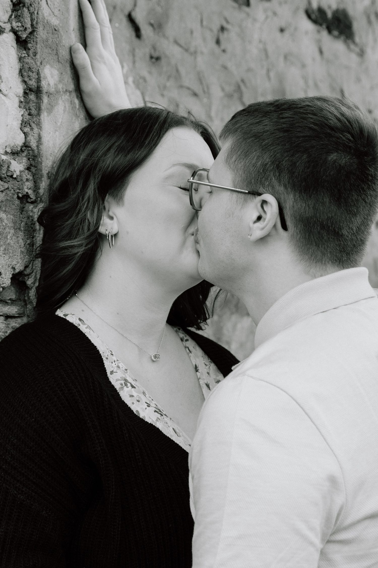 A romantic black and white photo of a couple sharing a tender kiss against a textured wall.
