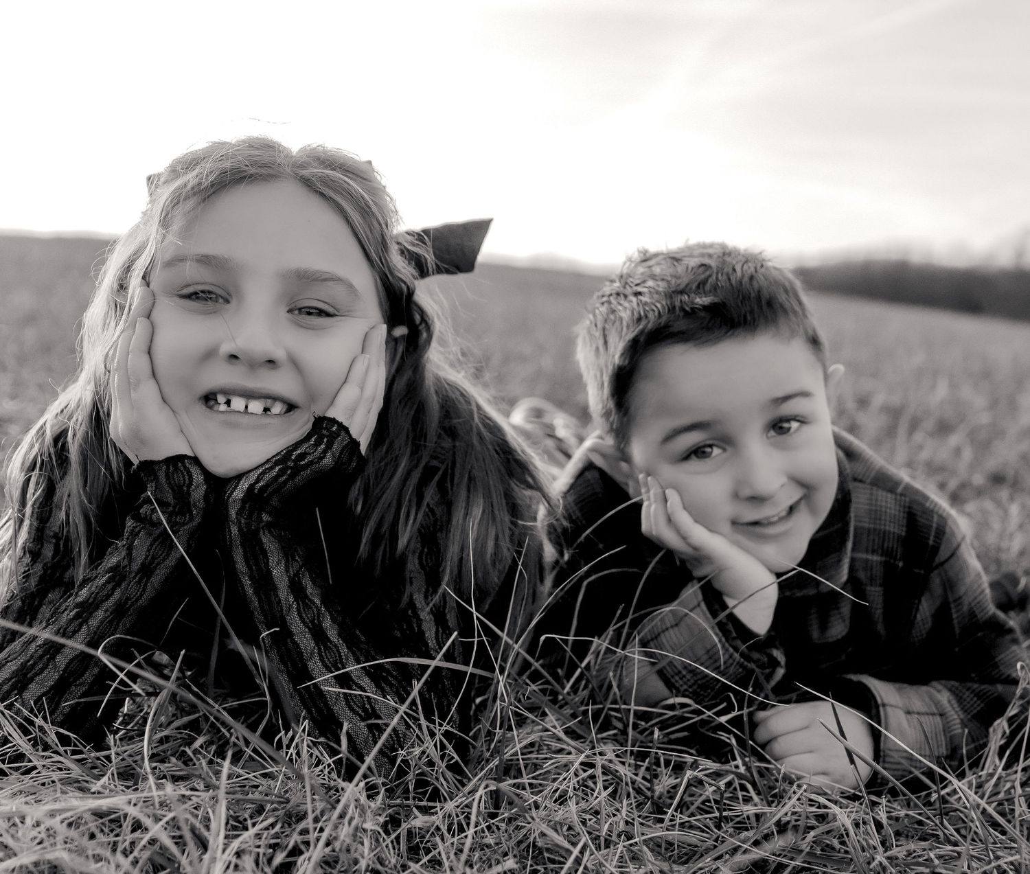 Two young children laying in tall grass outdoors on a sunny day captured in black and white photography. Cecil County Photographer