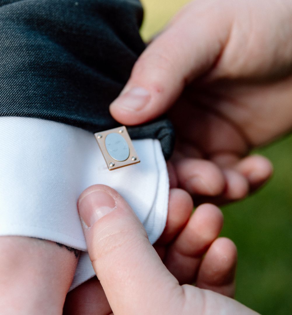 Close up of hands adjusting a silver cufflink on a white dress shirt sleeve with dark jacket.