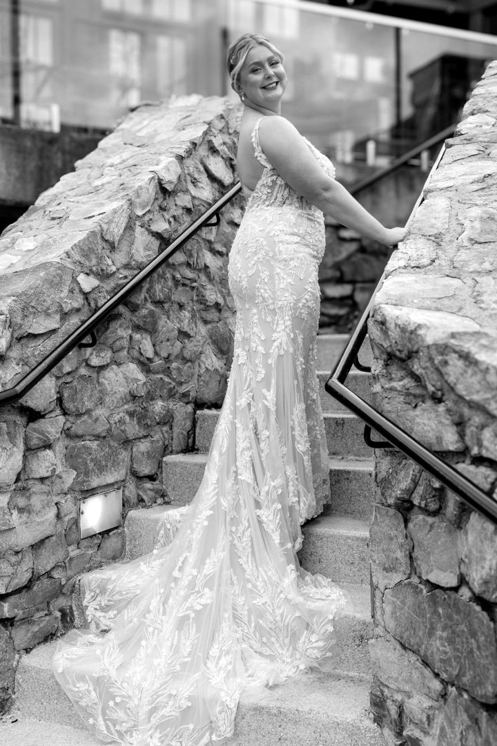 A person in a white wedding dress sits on stone steps against a rustic stone wall in a black and white photograph. Maryland Wedding.