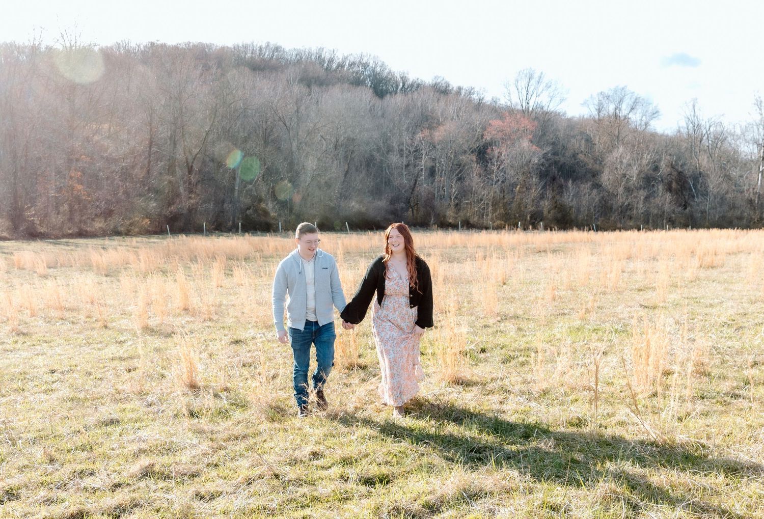 Two people walk hand in hand through a sun-drenched meadow as the golden light illuminates the serene winter landscape.