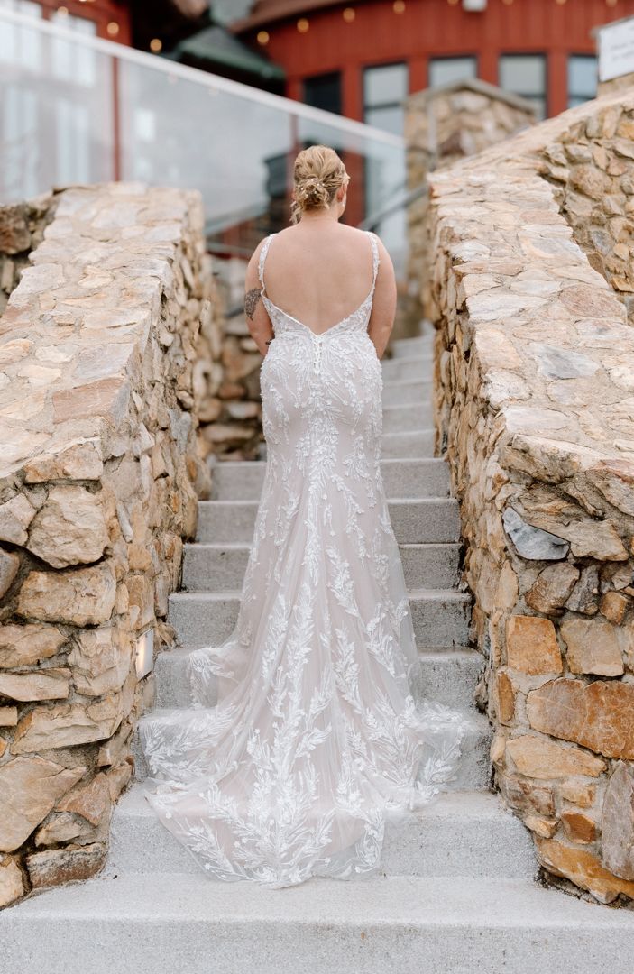 A delicate bridal gown with lace detailing sits on stone steps against a rustic rock wall.