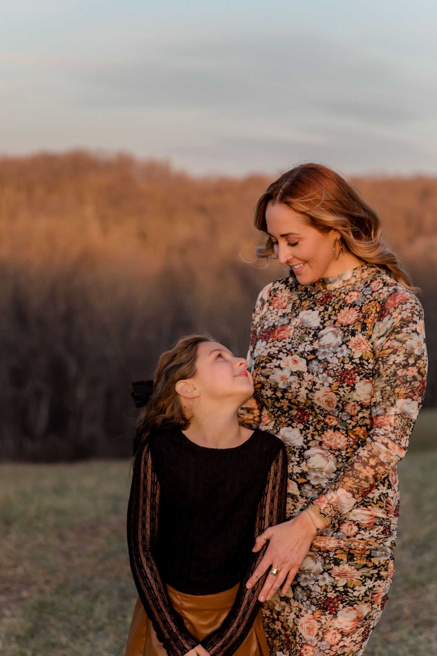 A heartfelt moment between parent and child wearing floral dress and black top in an autumn field at sunset.