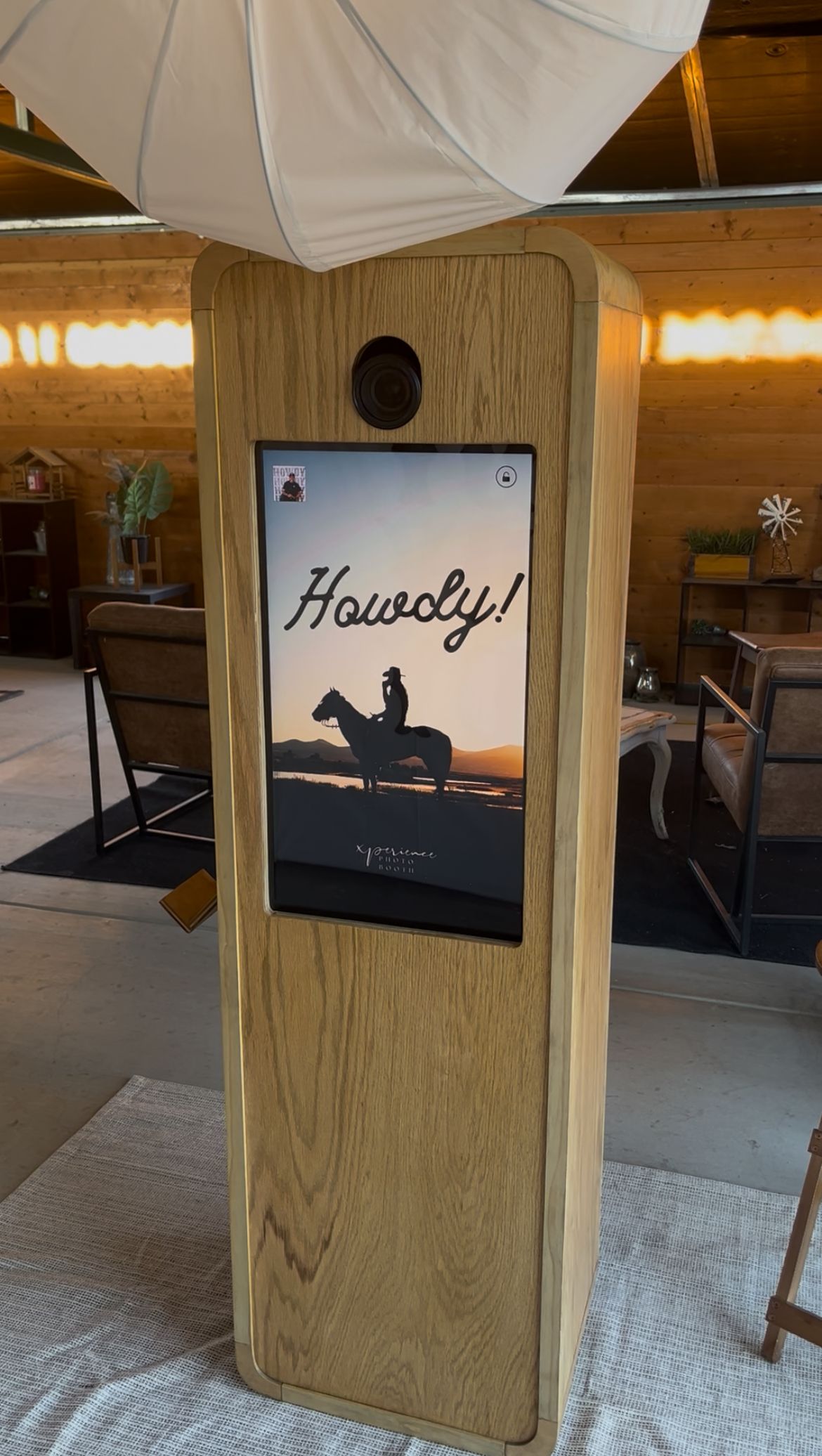 A wooden display stand shows a digital screen with a cowboy silhouette and 'Howdy!' text in a rustic interior setting.