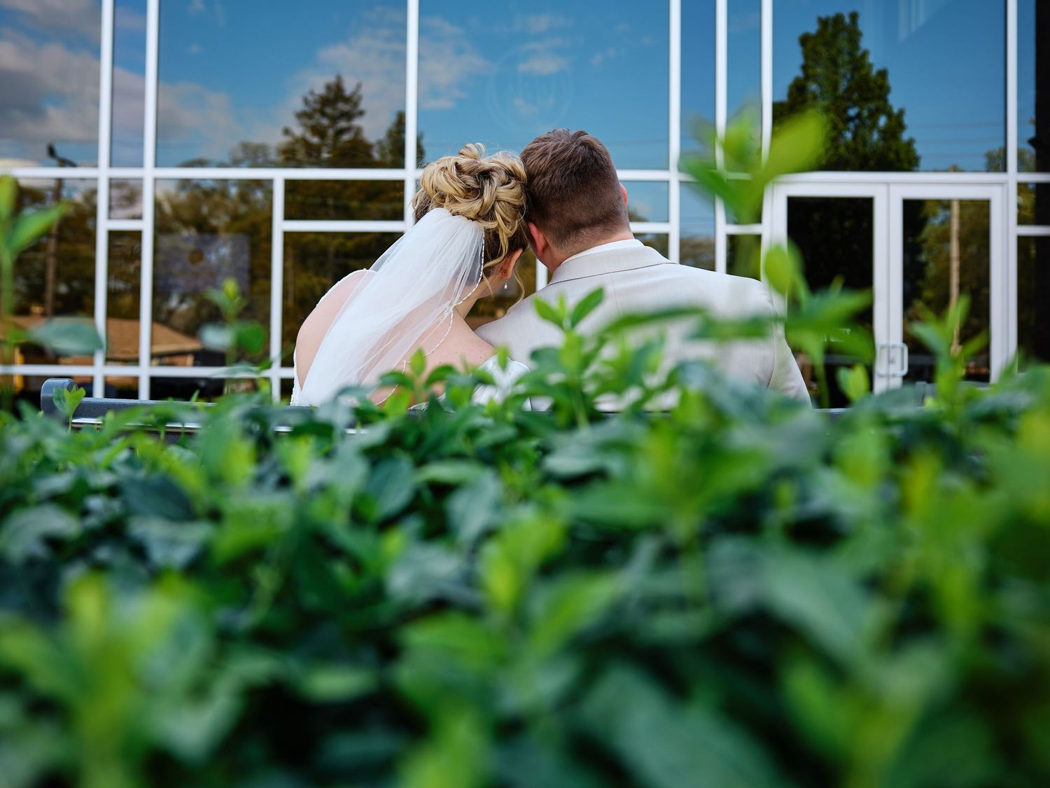 A bride and groom share a romantic moment in a lush garden, surrounded by green hedges and a white lattice fence.