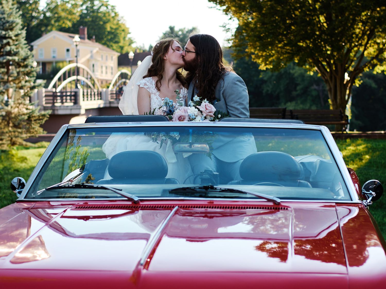 A romantic couple shares a tender moment in a red convertible car parked in a scenic location at sunset.