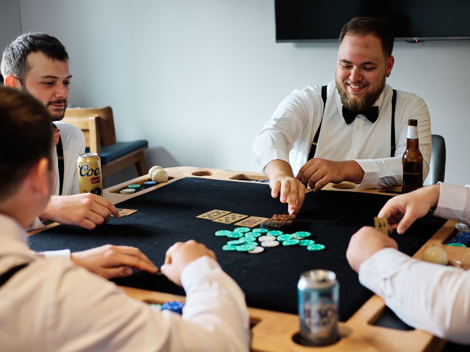 People gathered around a black table playing poker with teal chips and beverages during a casual gaming session.