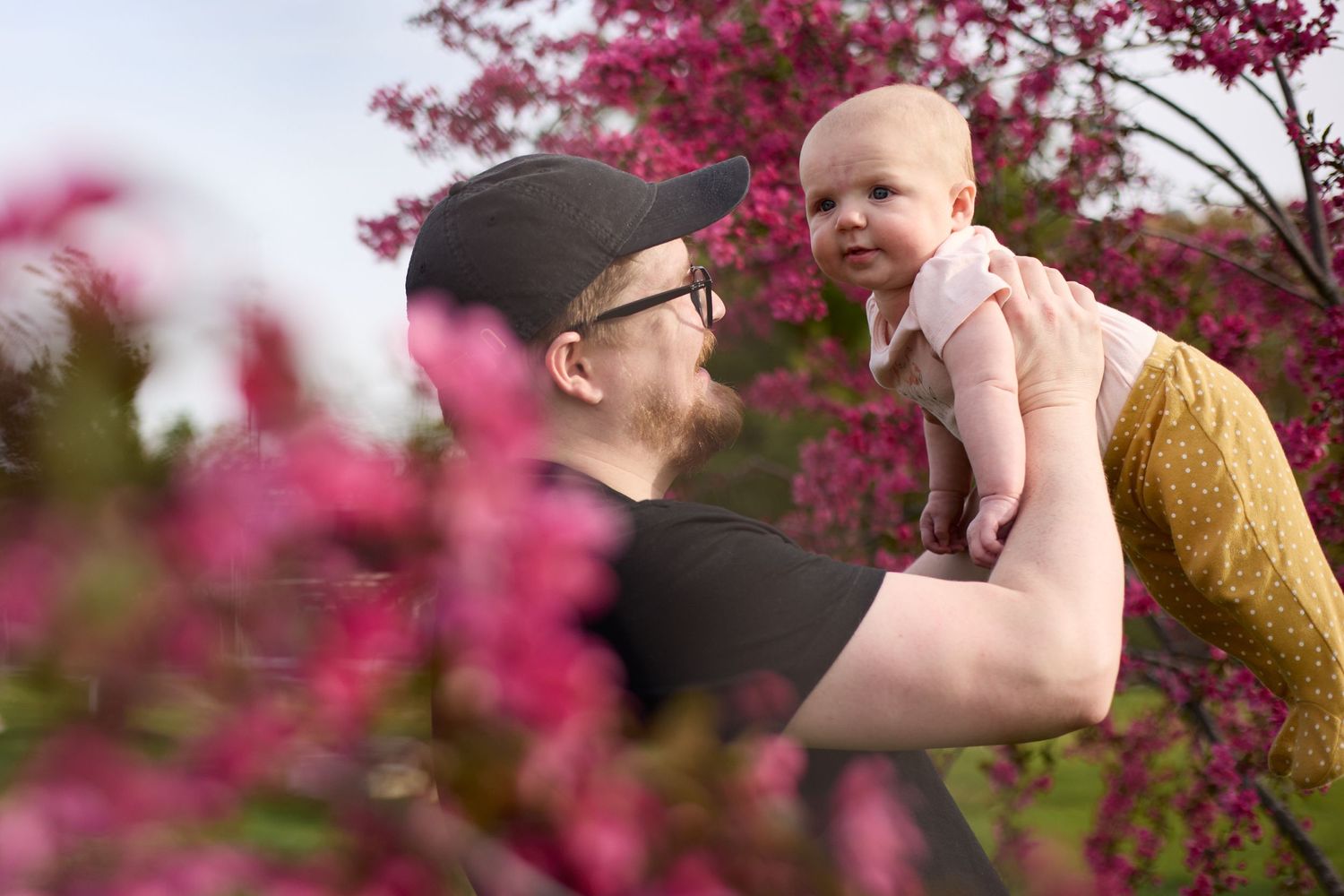 A tender parent-child moment captured among vibrant pink flowering branches in springtime.