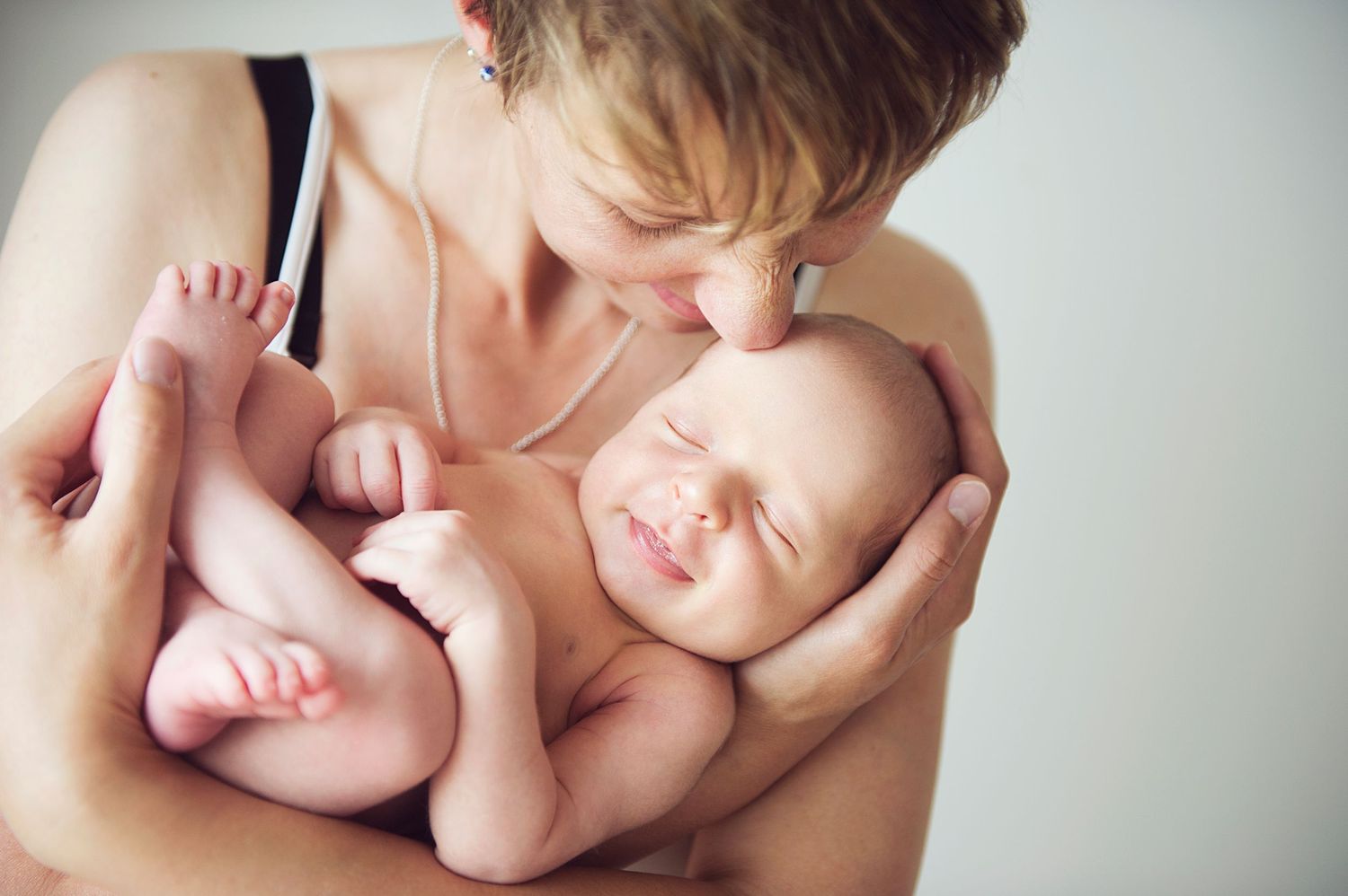 A tender moment between parent and newborn baby showing gentle skin-to-skin contact against a light background. Newborn photo session