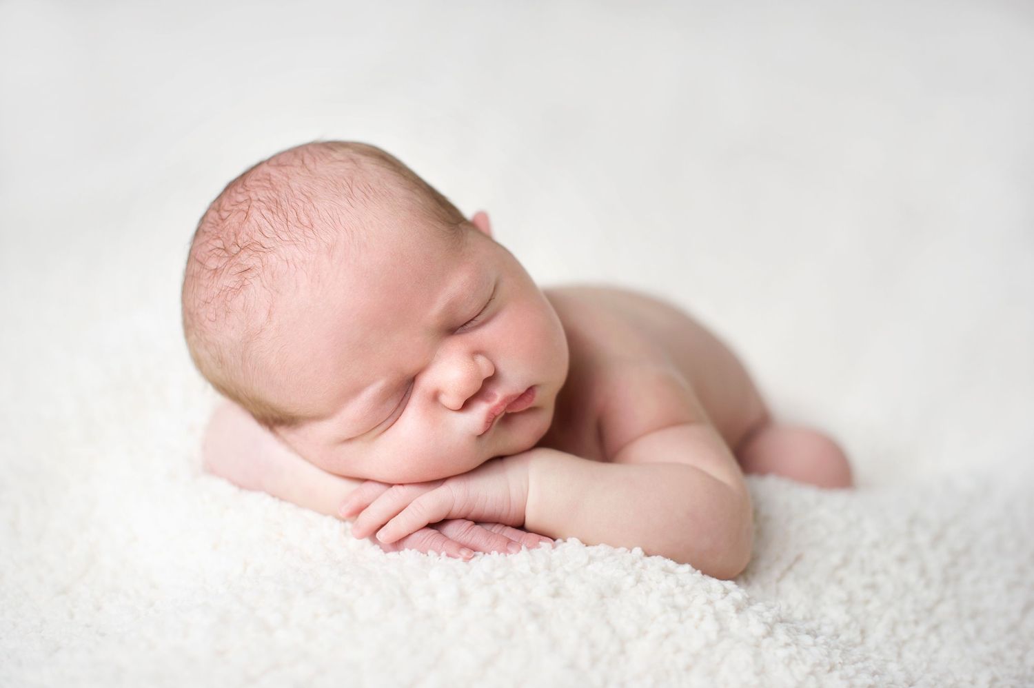 Peaceful sleeping newborn baby curled up on soft white textured blanket in gentle studio lighting. Newborn session with Phoebe Lee Photo.