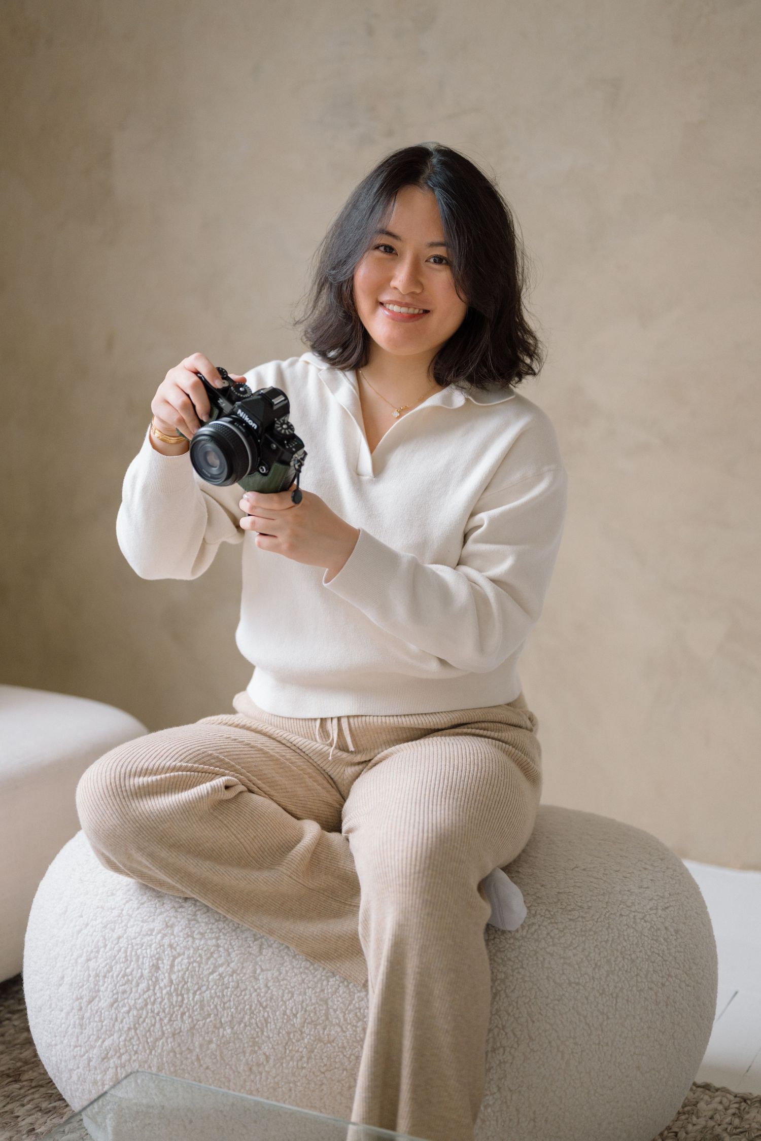 Phoebe Lee, a Toronto-based newborn and family photographer, smiling while holding her camera in a studio setting.