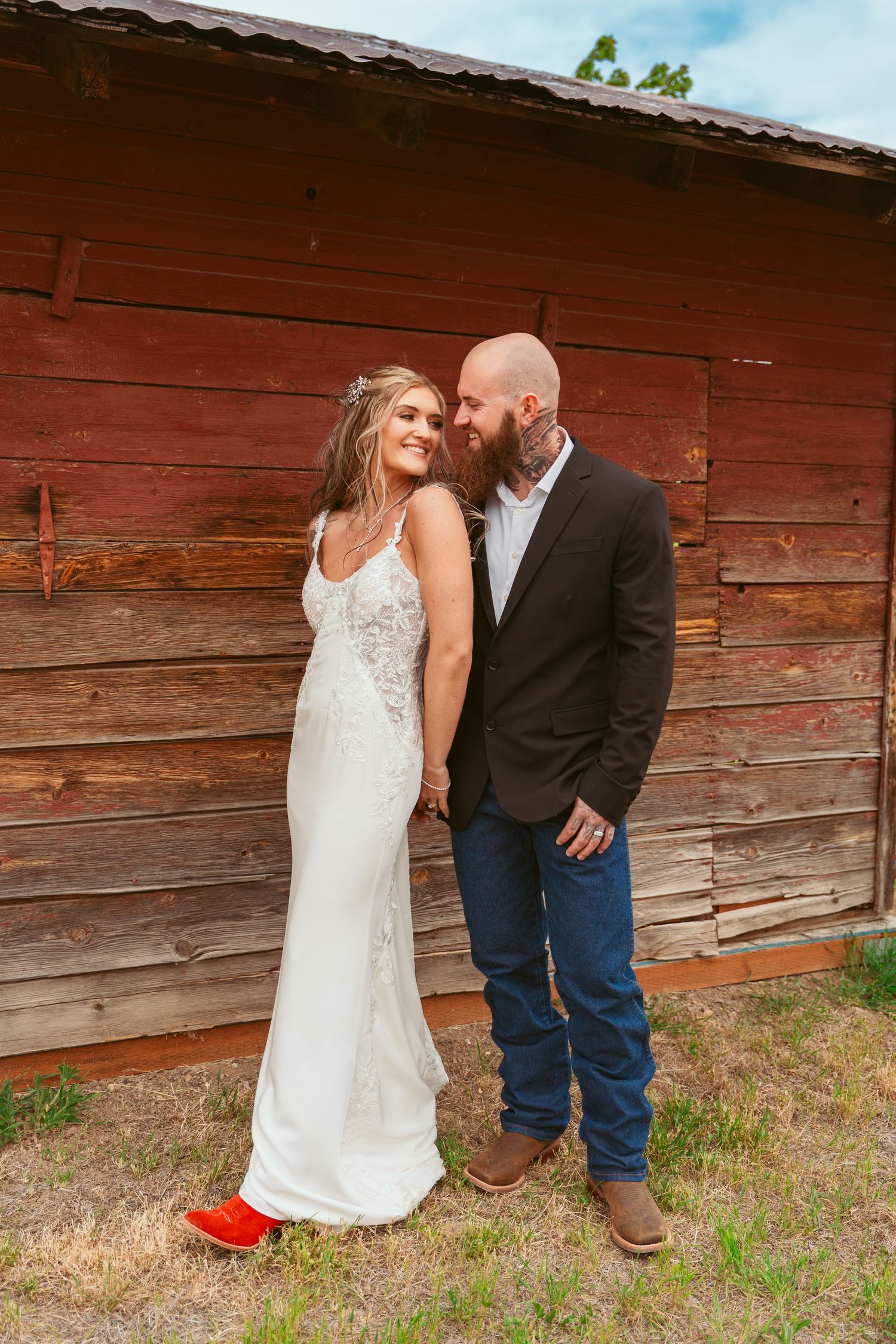 A couple posing together against a rustic red barn in a romantic countryside wedding photoshoot.