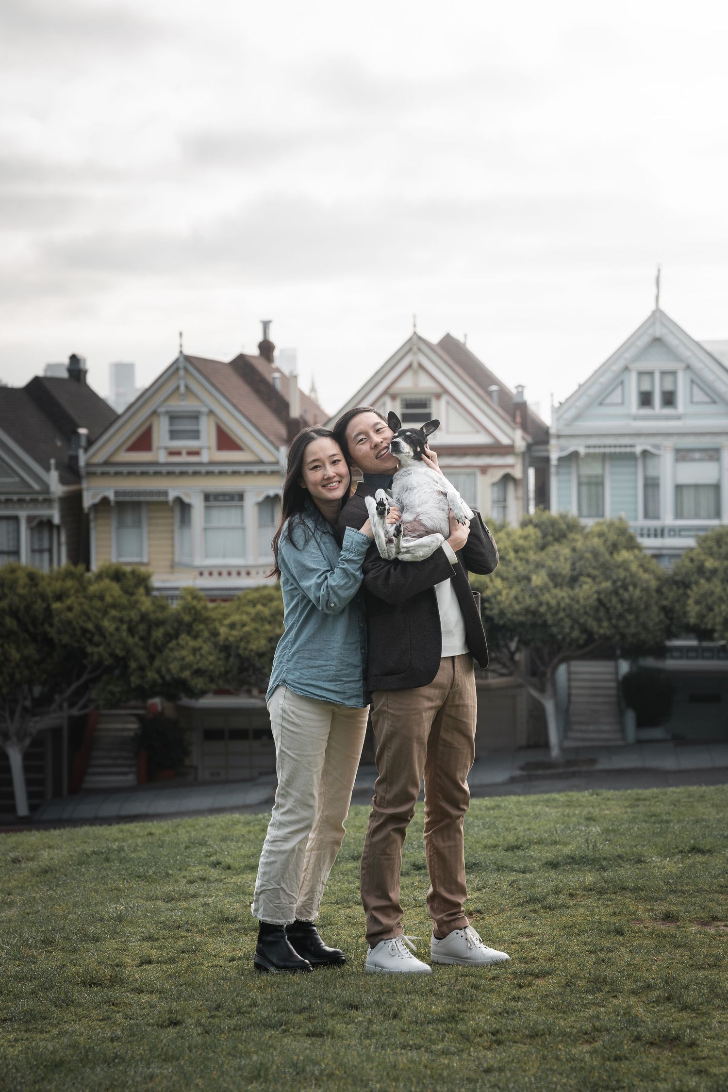 Smiling couple holding small dog in front of the iconic Painted Ladies in San Francisco.