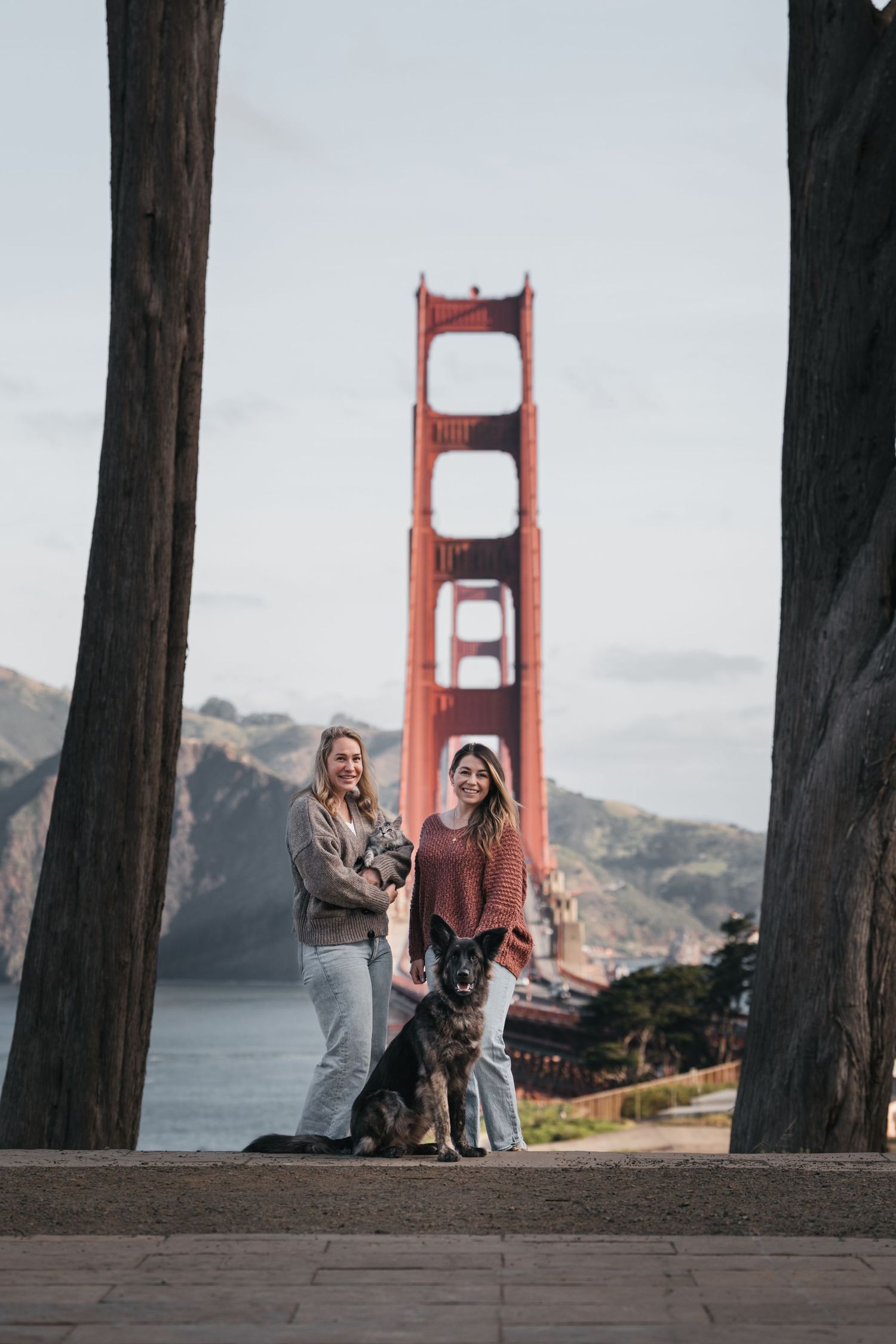 Two women and a German Shepherd dog pose in front of the Golden Gate Bridge in San Francisco.