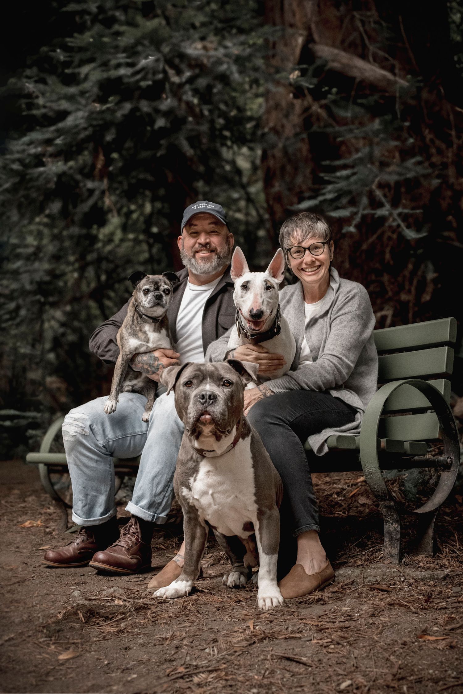 Family portrait with two humans and three dogs on a bench in Leona Heights Oakland, all smiling at the camera.