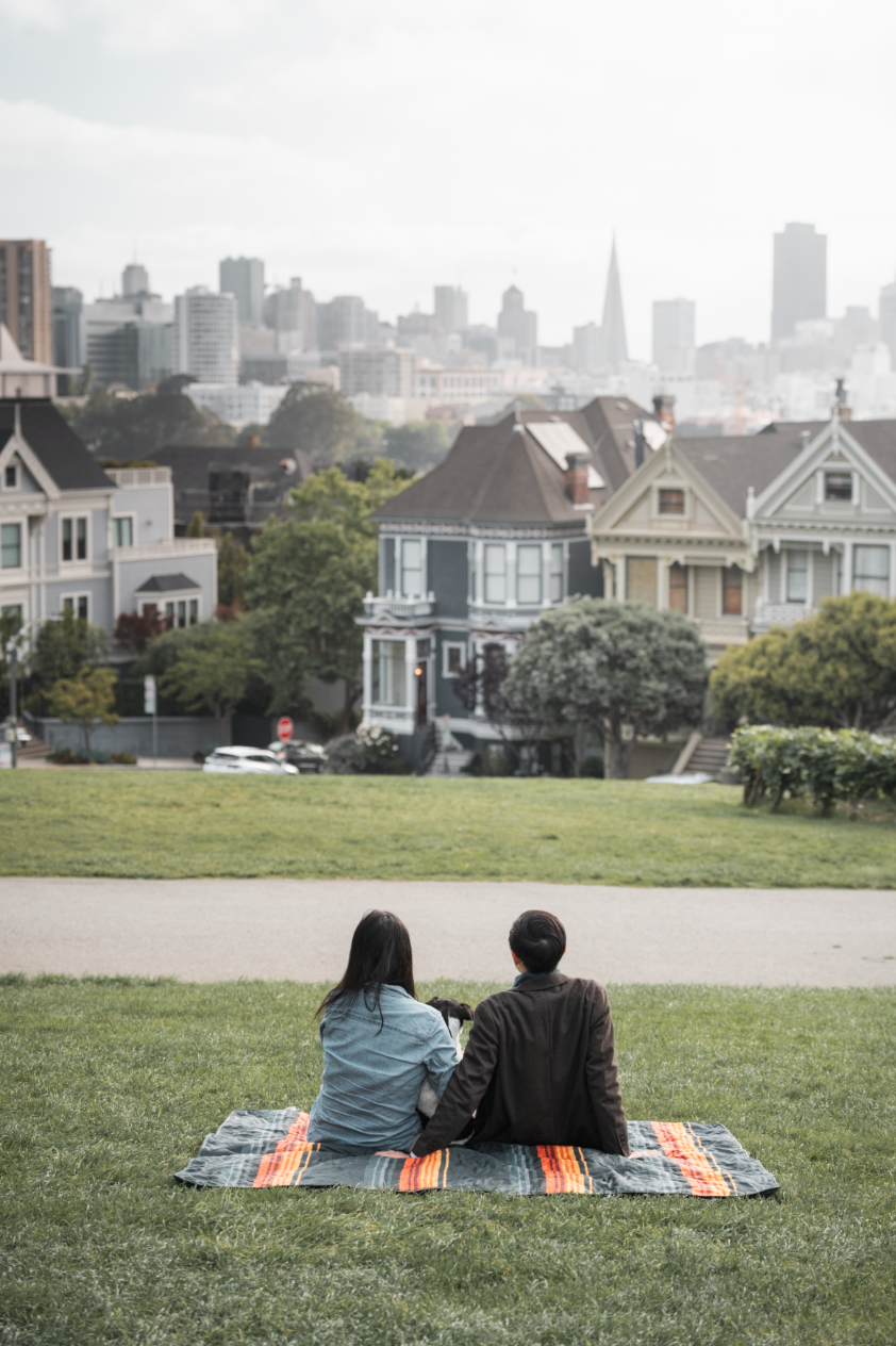 Couple sitting on blanket in Alamo Square Park with Painted Ladies and San Francisco skyline.