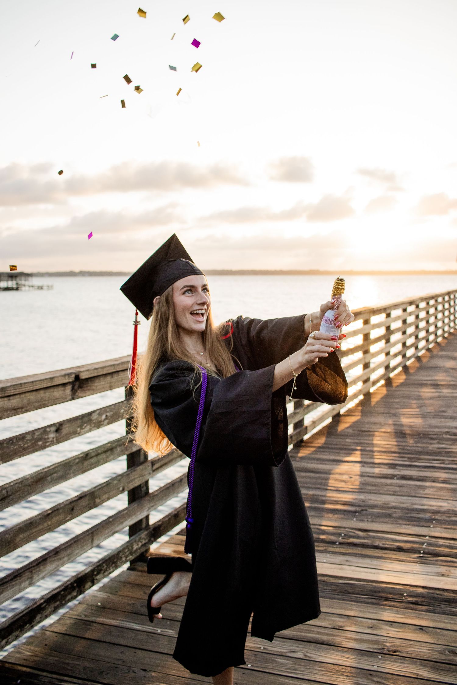 Graduation photo of a girl on a bridge, popping confetti while wearing her cap and gown.