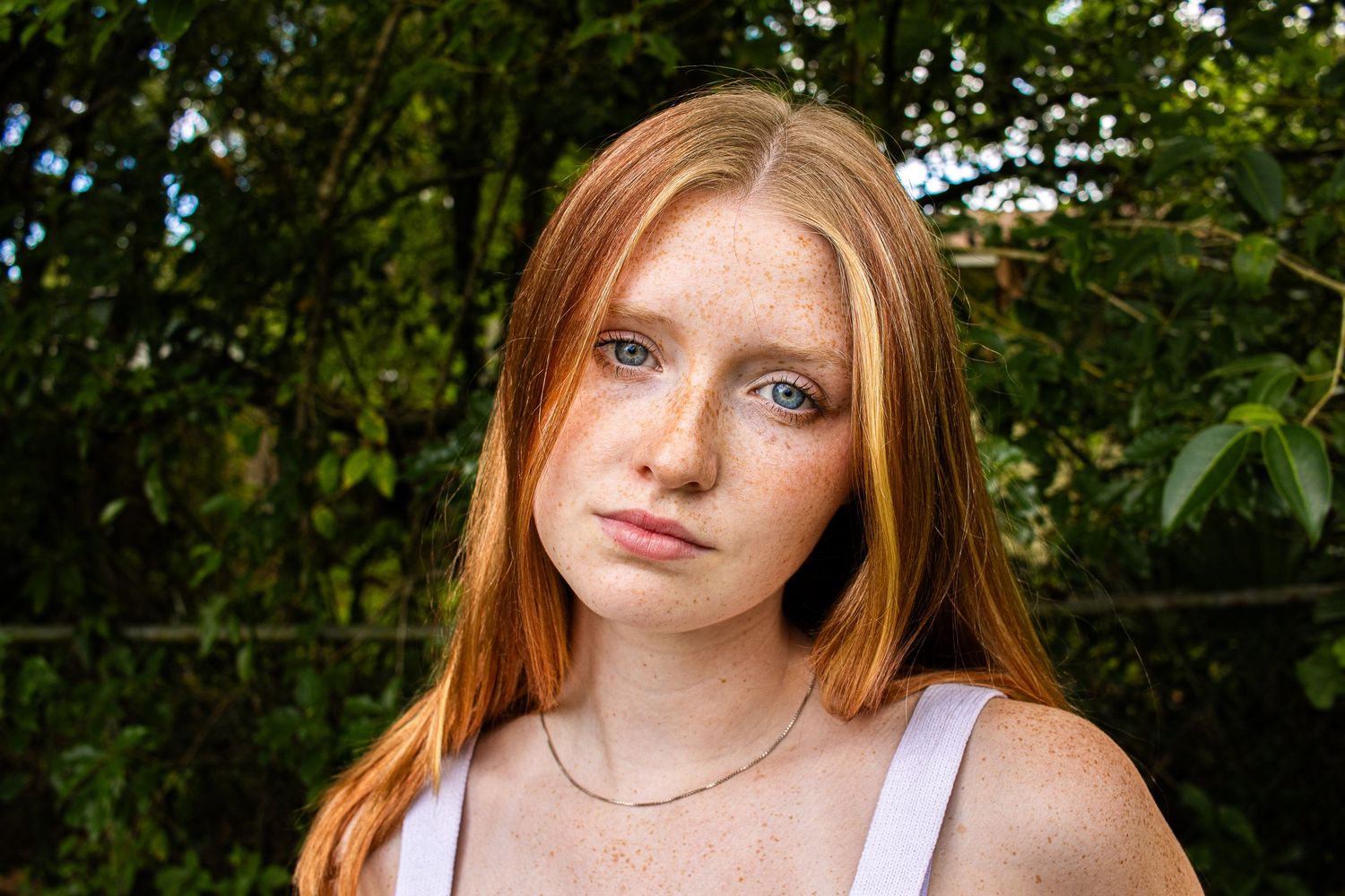 Close-up of a freckled red-haired model with a serious expression, captured outdoors.