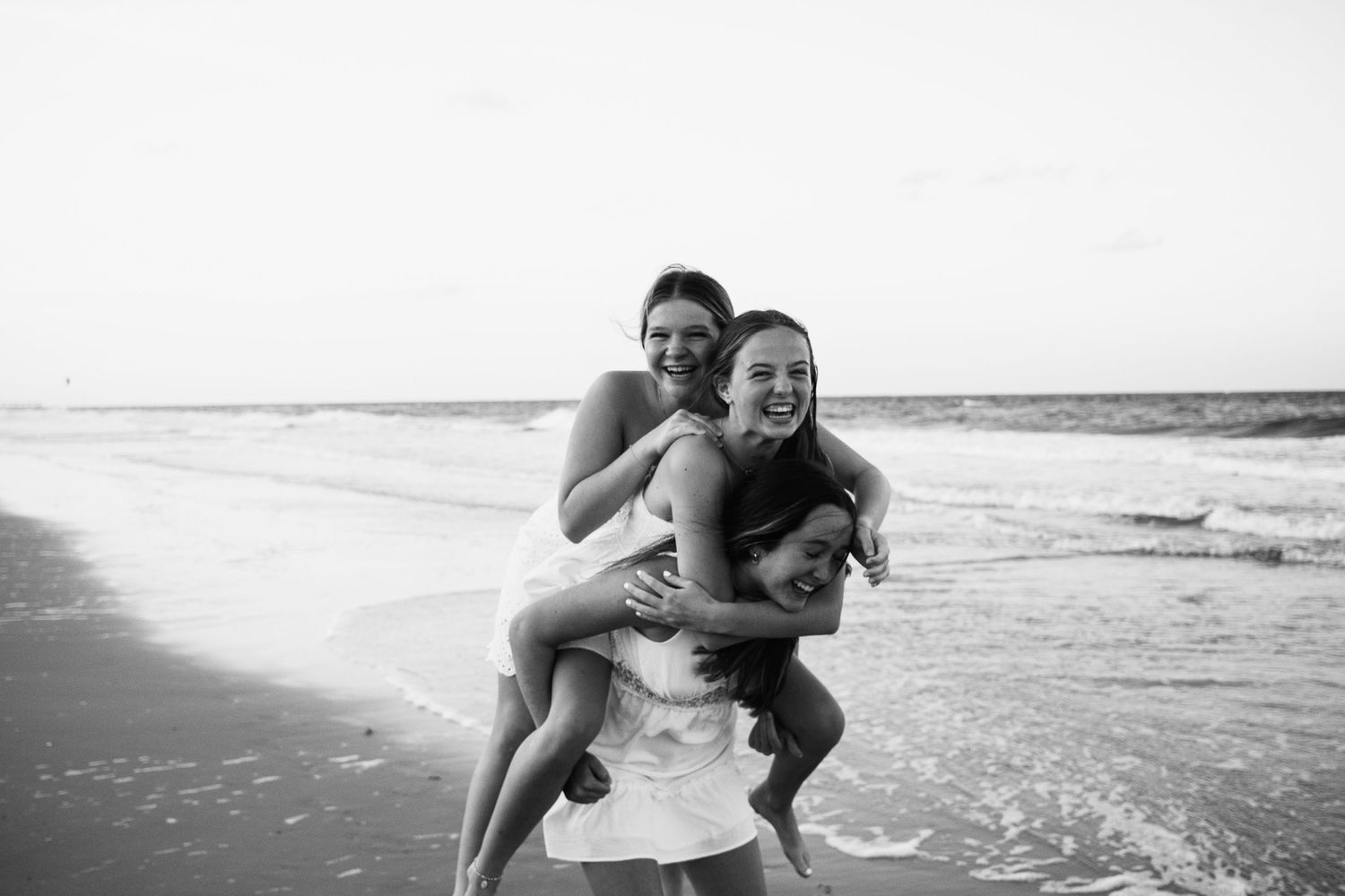 Three friends on the beach trying to do a group piggyback, laughing and having fun together.