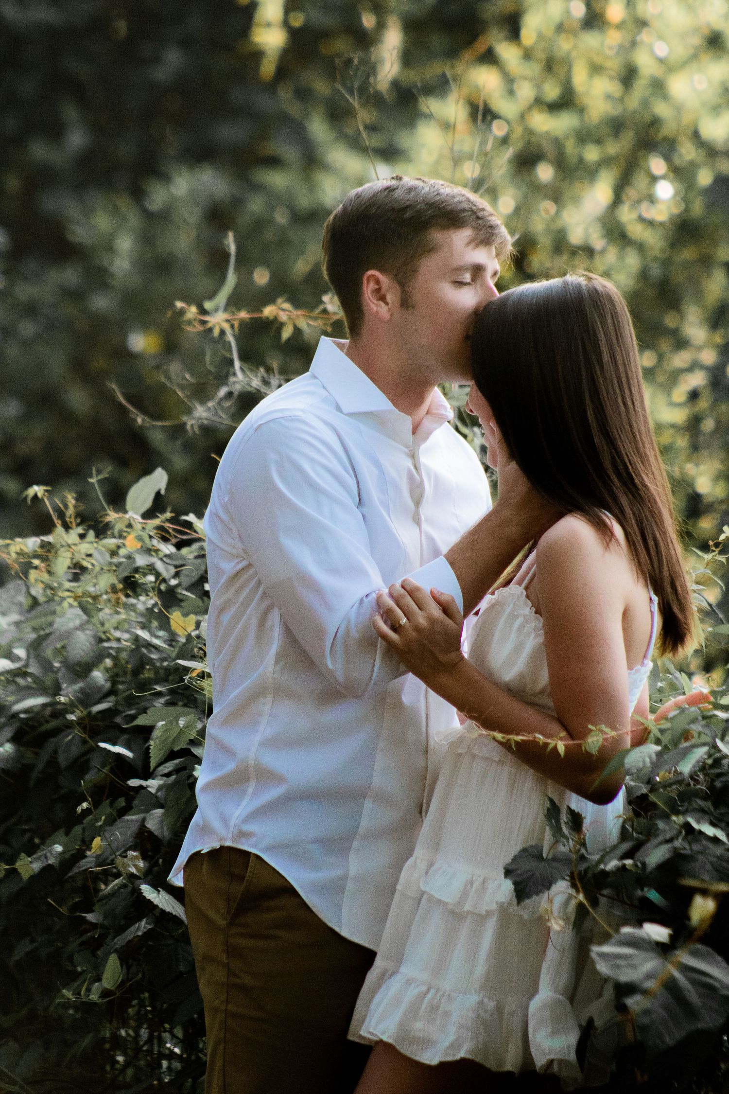 Engagement photo of a man kissing his fiancée's forehead as she holds onto his arms, capturing a tender and loving moment.