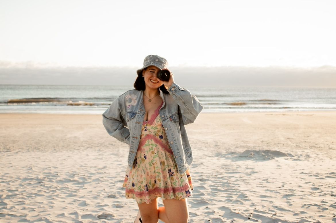 Profile picture for Kinderly Photography on the beach, with the photographer holding a camera up to their eye.