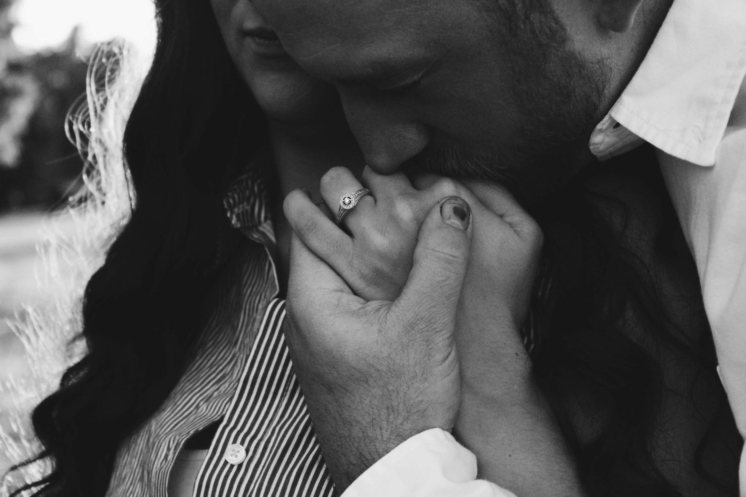 Close-up of a groom kissing his bride's hand, focusing on her wedding ring, with their faces out of frame.