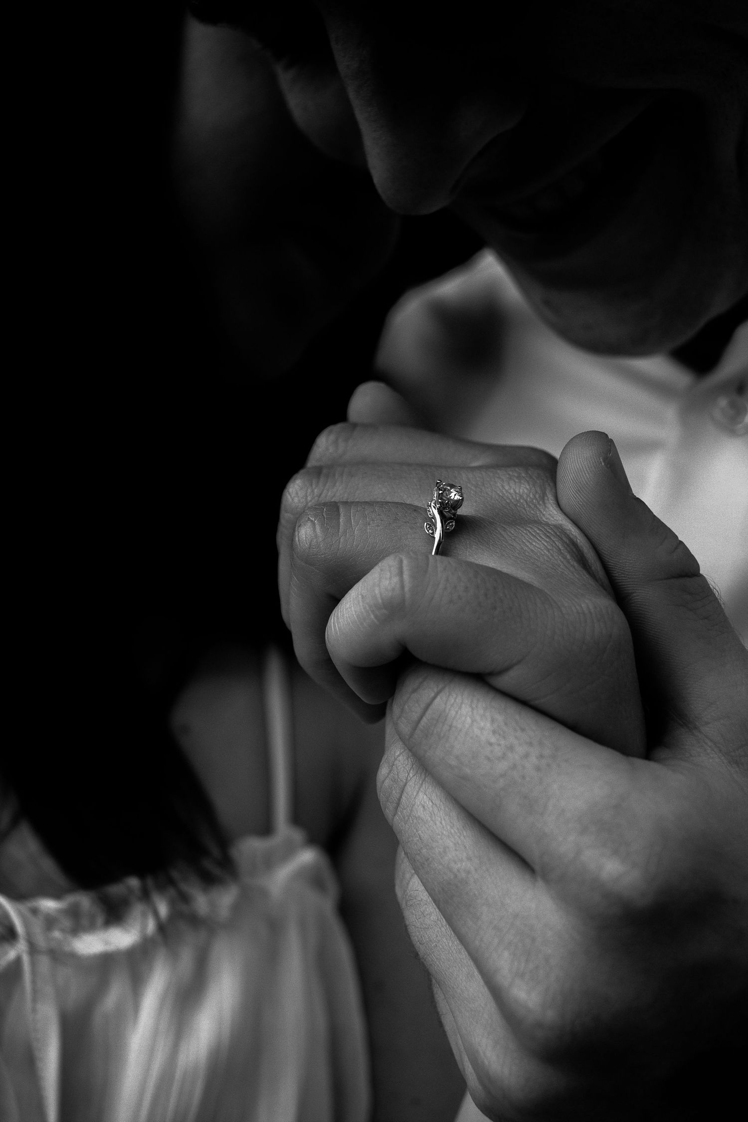 Black and white close-up of hands holding each other, showcasing the engagement ring.