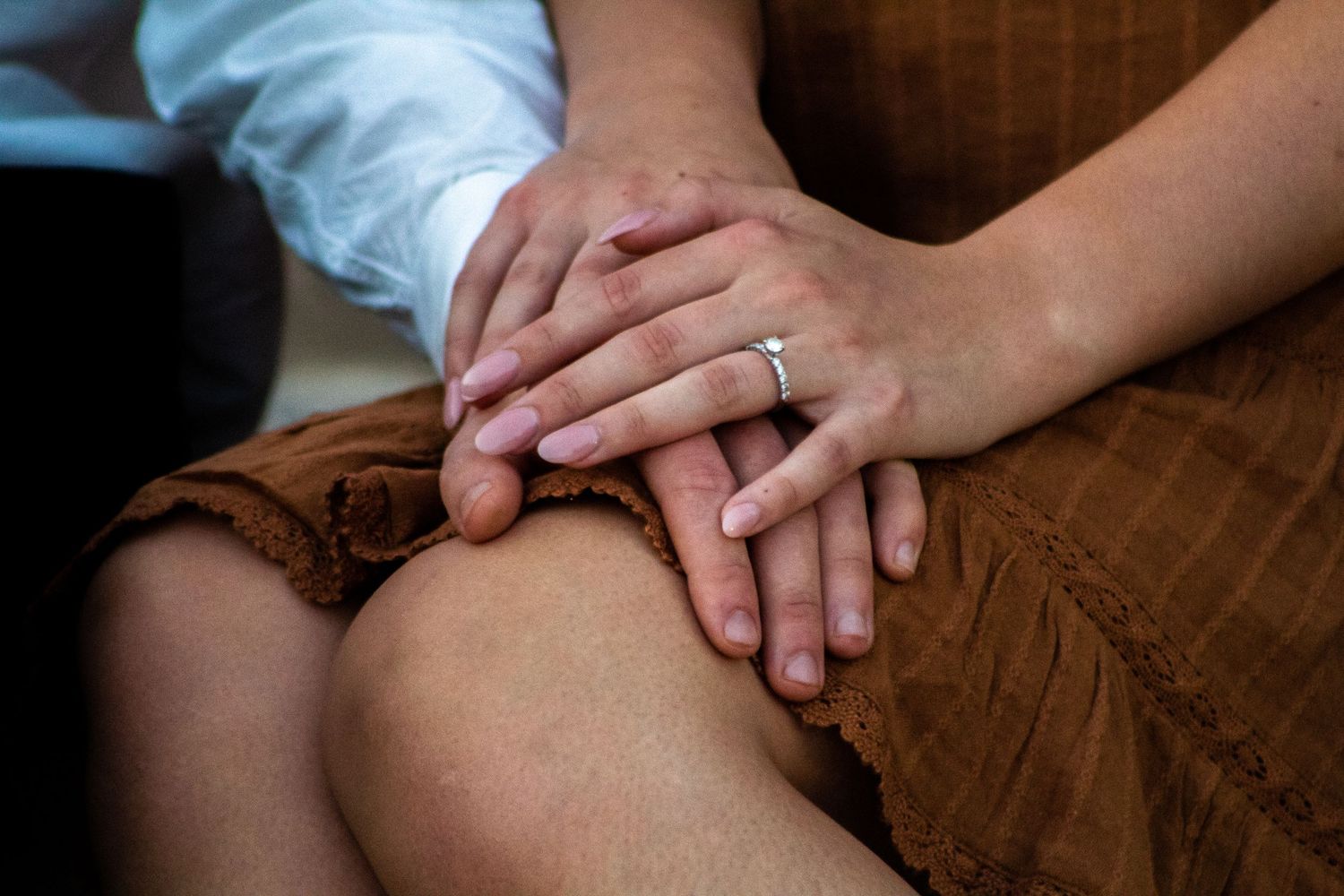 Close-up of an engaged couple's hands stacked together, highlighting the fiancée's engagement ring.