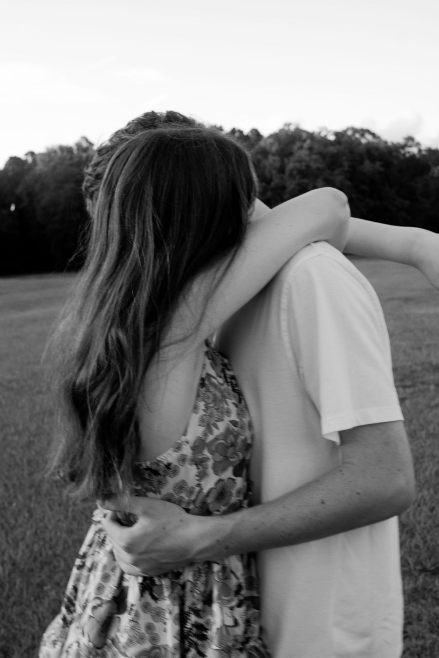 Girlfriend hugging her boyfriend by wrapping her arms around his neck, as he buries his face in hers while holding her waist.