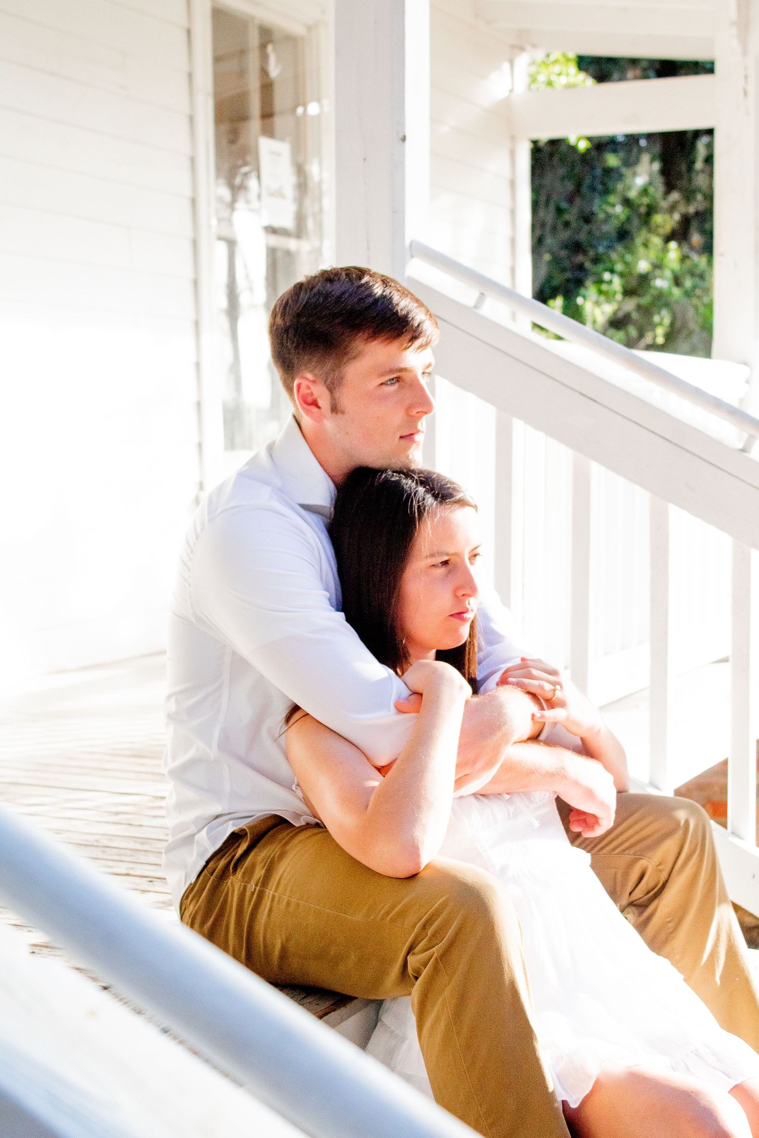 Engagement photo of a couple sitting on stairs, the woman laying back on her fiancé, holding his arms in a serious, intimate moment.