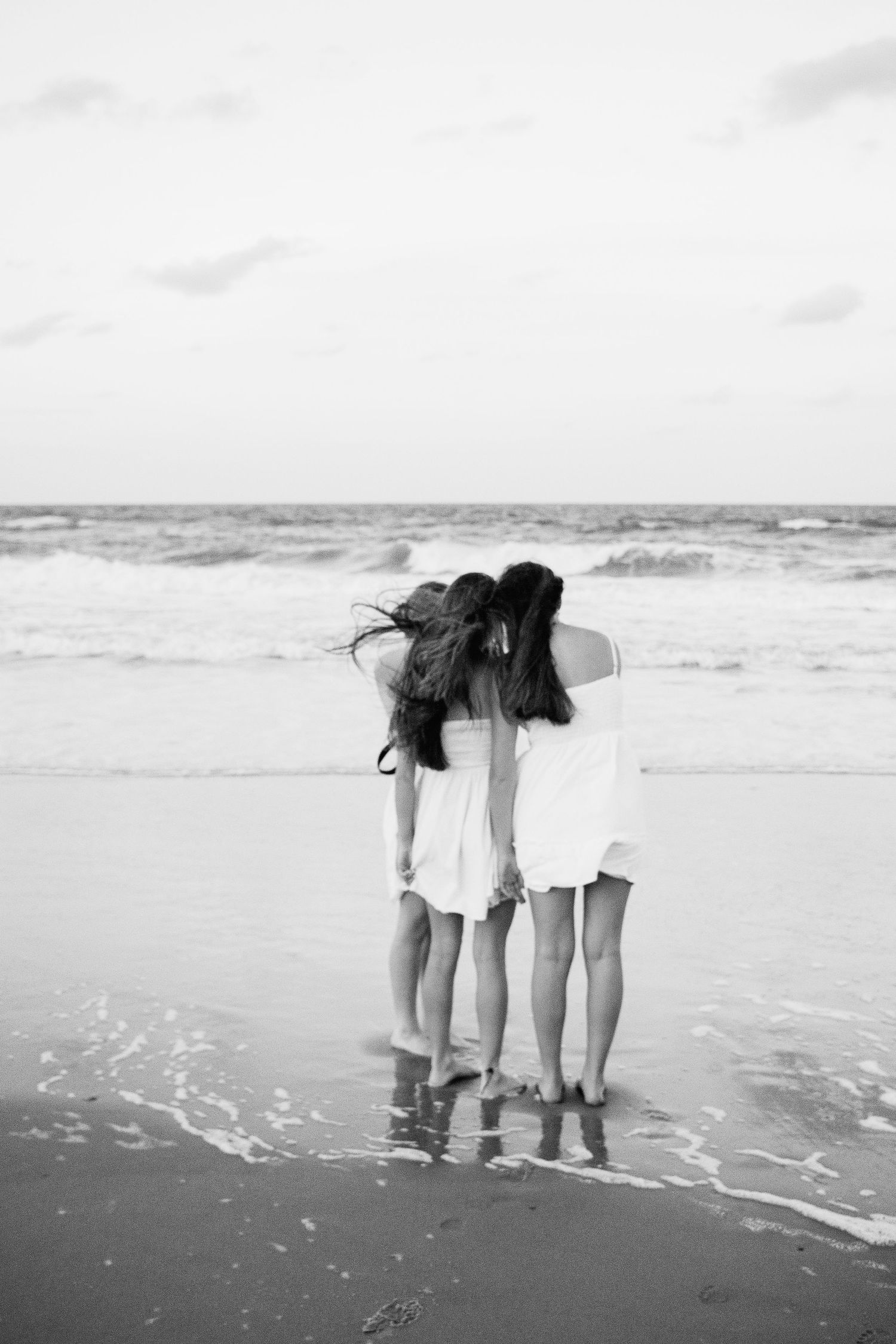 Photo of three best friends standing with their backs to the camera, leaning into each other on the beach.