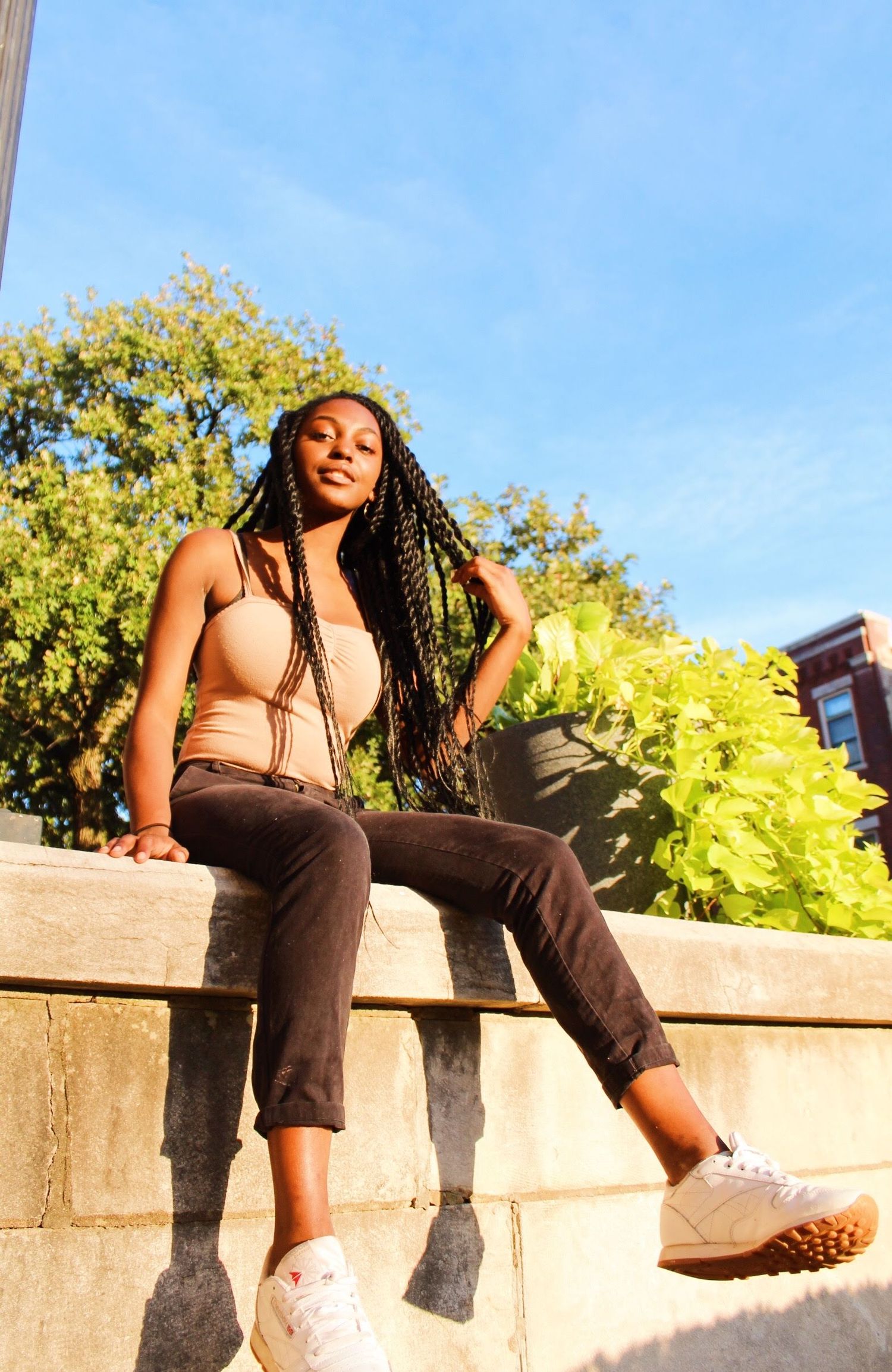 Black model sitting on a brick wall, with the camera panned up towards her and the sky as she grabs her hair.
