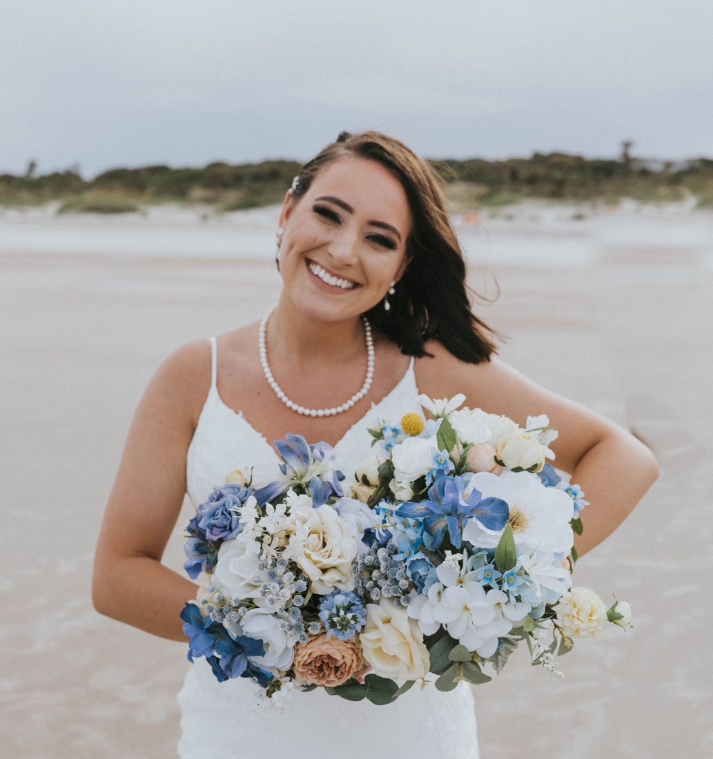 Wedding photo of Kinderly Photography holding her bridal bouquet and smiling, capturing a joyful and elegant moment.