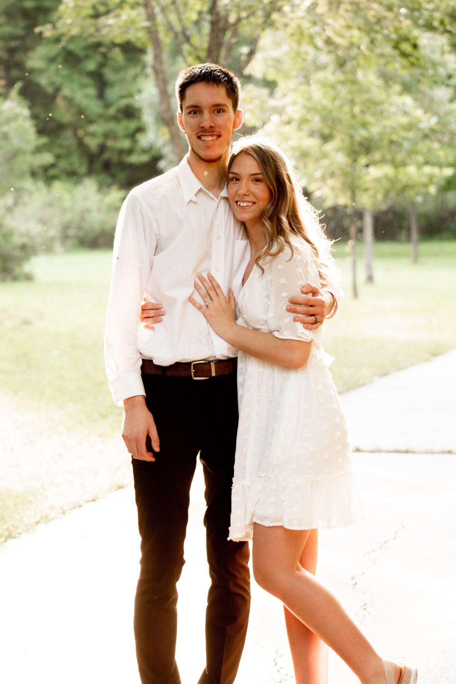 Engagement photo of a couple standing together, with the fiancé's arms wrapped around his fiancée in a simple and classic pose.