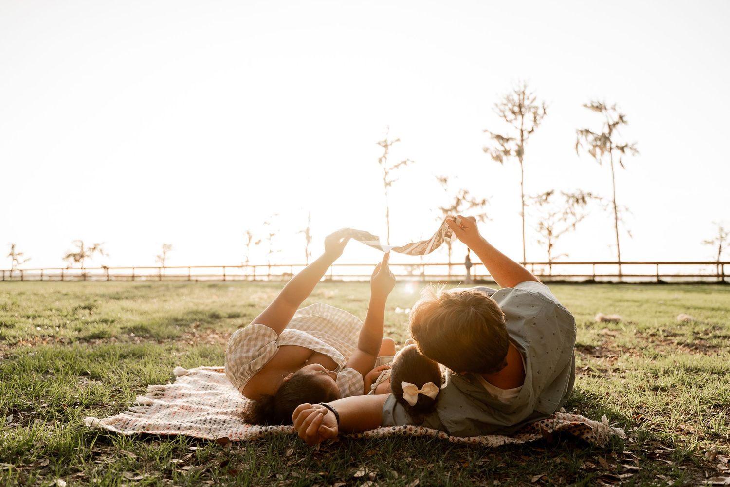 mom and dad lying on picnic blanket with their daughter while they look at a sonogram welcoming their new addition soon.