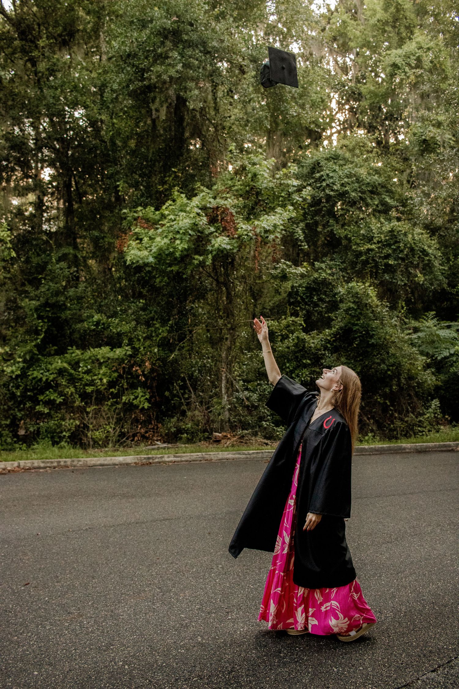 Graduation photo of a girl throwing her cap in the air, looking up at it with a joyful expression.