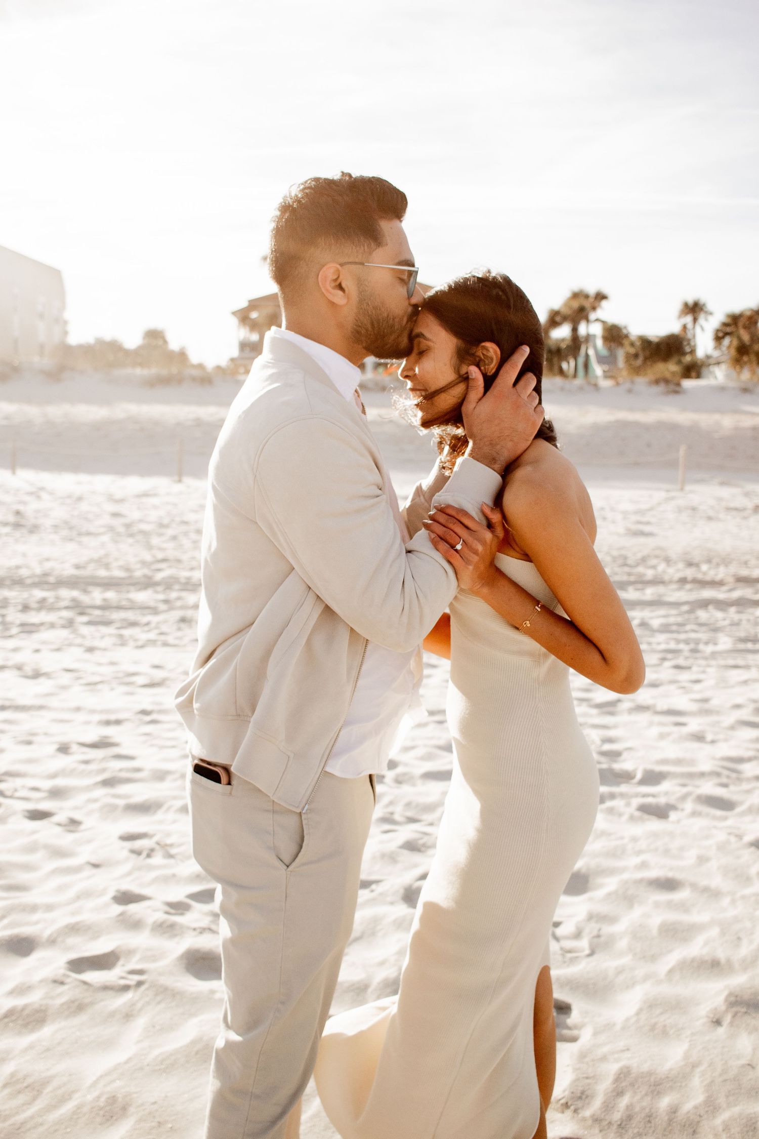 Fiancé kissing his fiancée on the forehead during their engagement photo session on the beach at sunset.