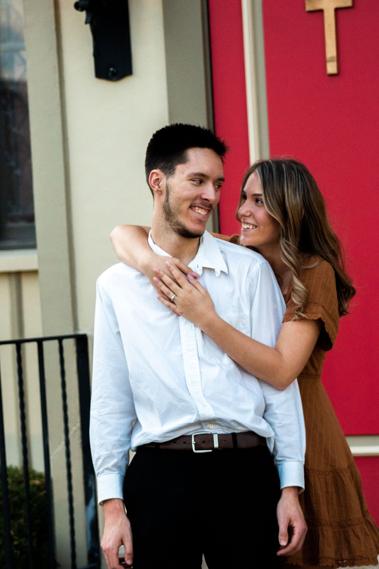 Engagement photo of a woman wrapping her arms around her fiancé from behind, as he looks at her with a smile.