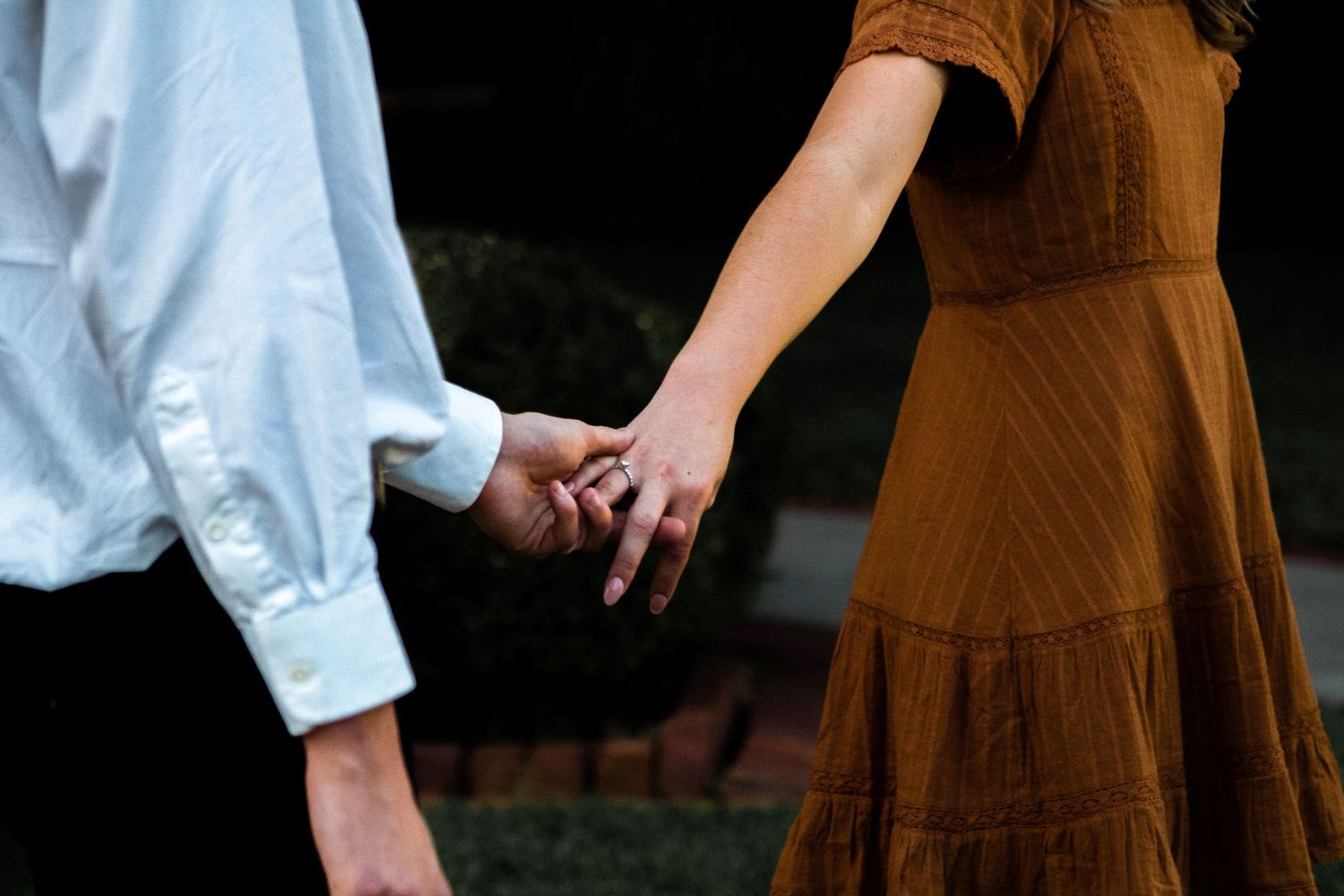 Girl pulling her engaged fiancé, proudly showing off her engagement ring as she leads him forward.