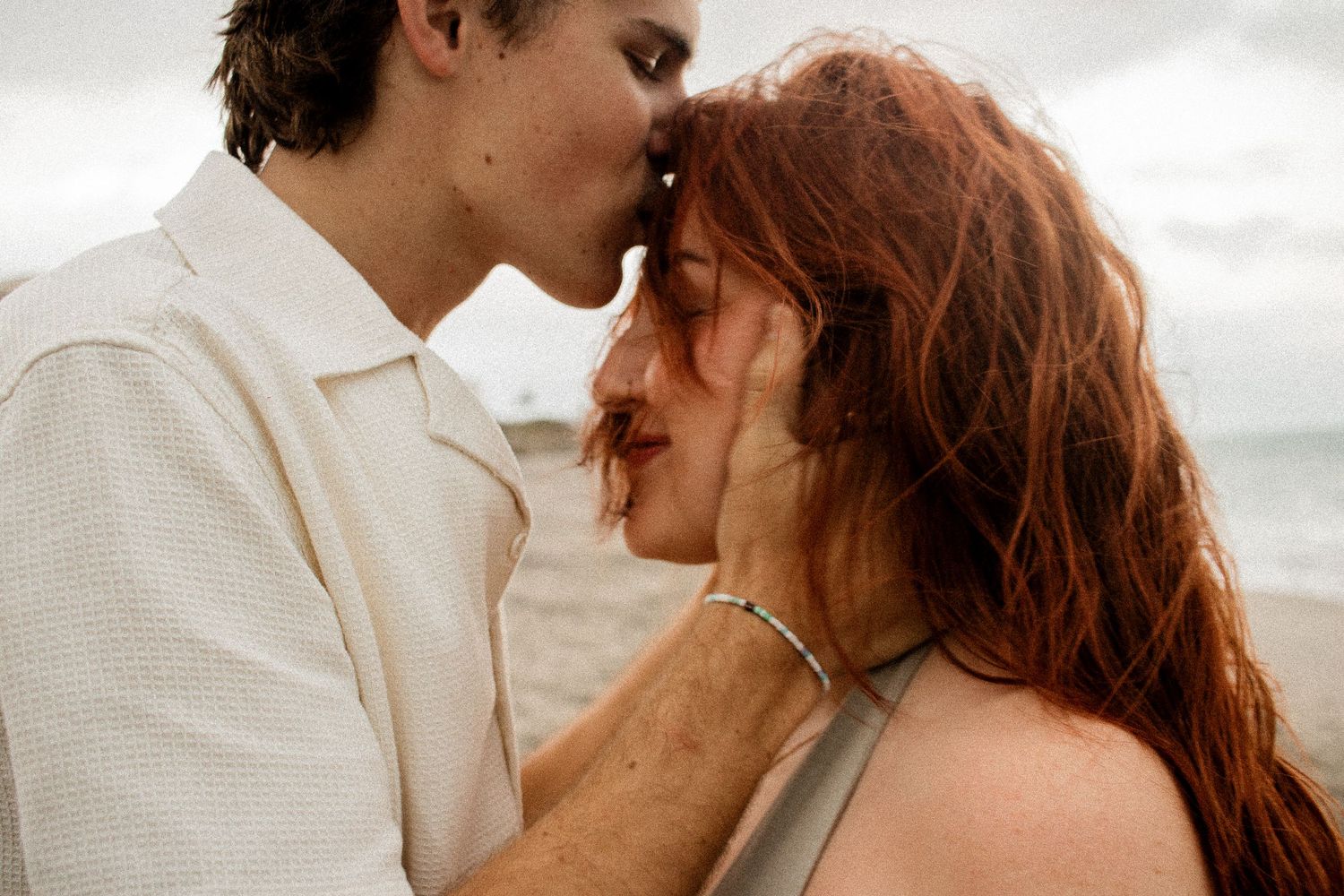 Forehead kiss, soft smile, salty wind, and ocean air—love and calm collide in this dreamy beachside moment.