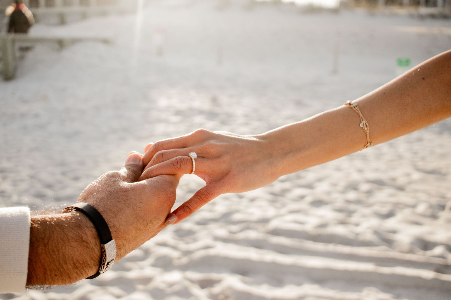 Couple walking hand-in-hand, with their hands held up to showcase the engagement ring.