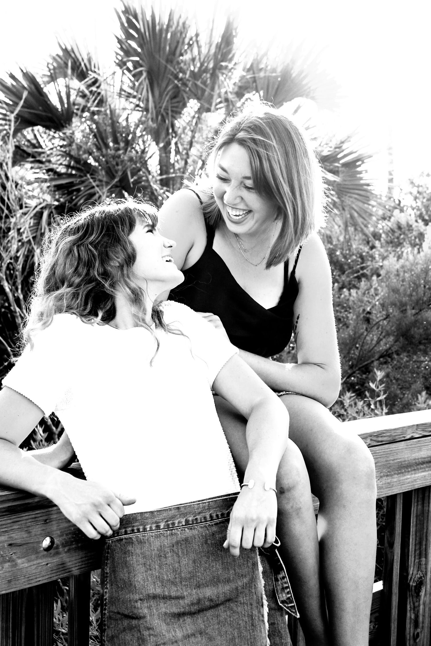 Two best friends laughing and looking at each other, one standing on a ledge while the other watches her, capturing a fun and joyful moment.