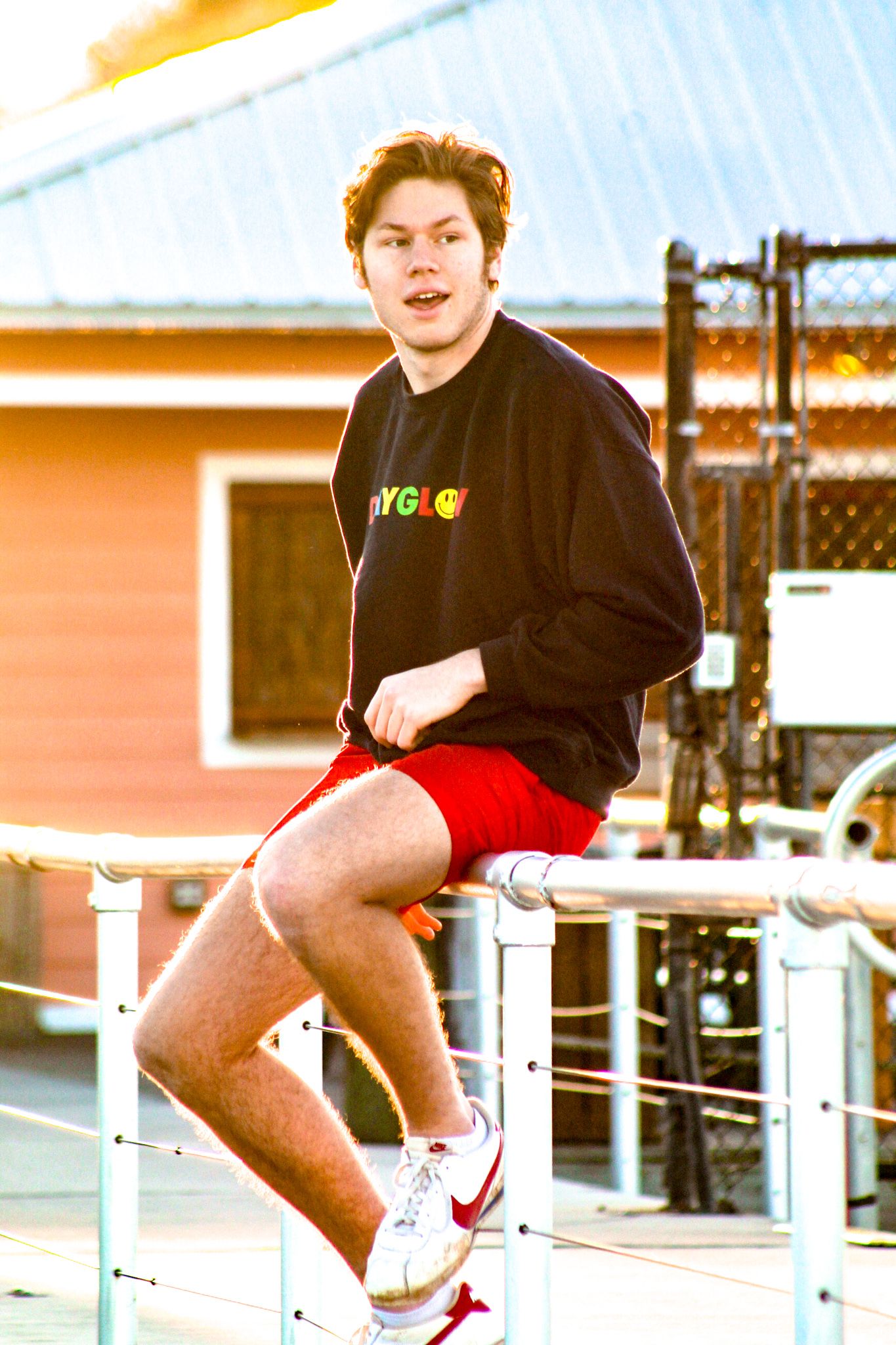 Male senior sitting on a fence surrounded by water, looking away during sunset for his graduation photos.