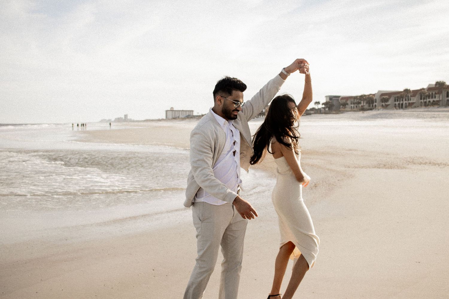 Newly engaged couple, man spinning his fiancée on the beach at sunset, capturing a joyful moment.
