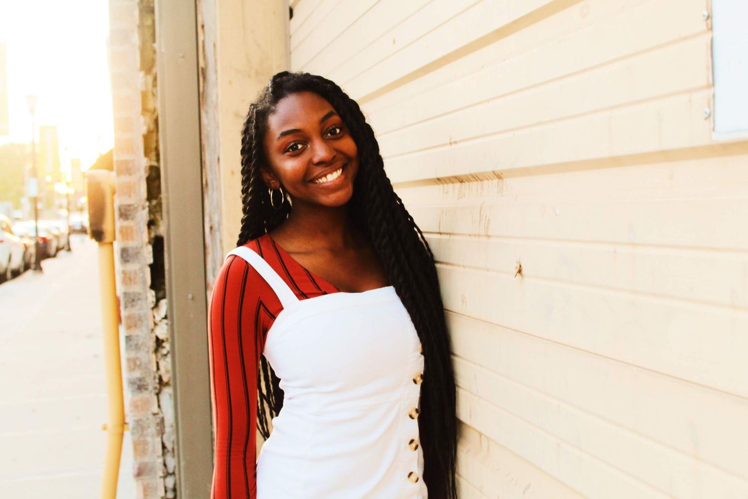 Graduation photo of a girl leaning on the side of a wall, smiling.
